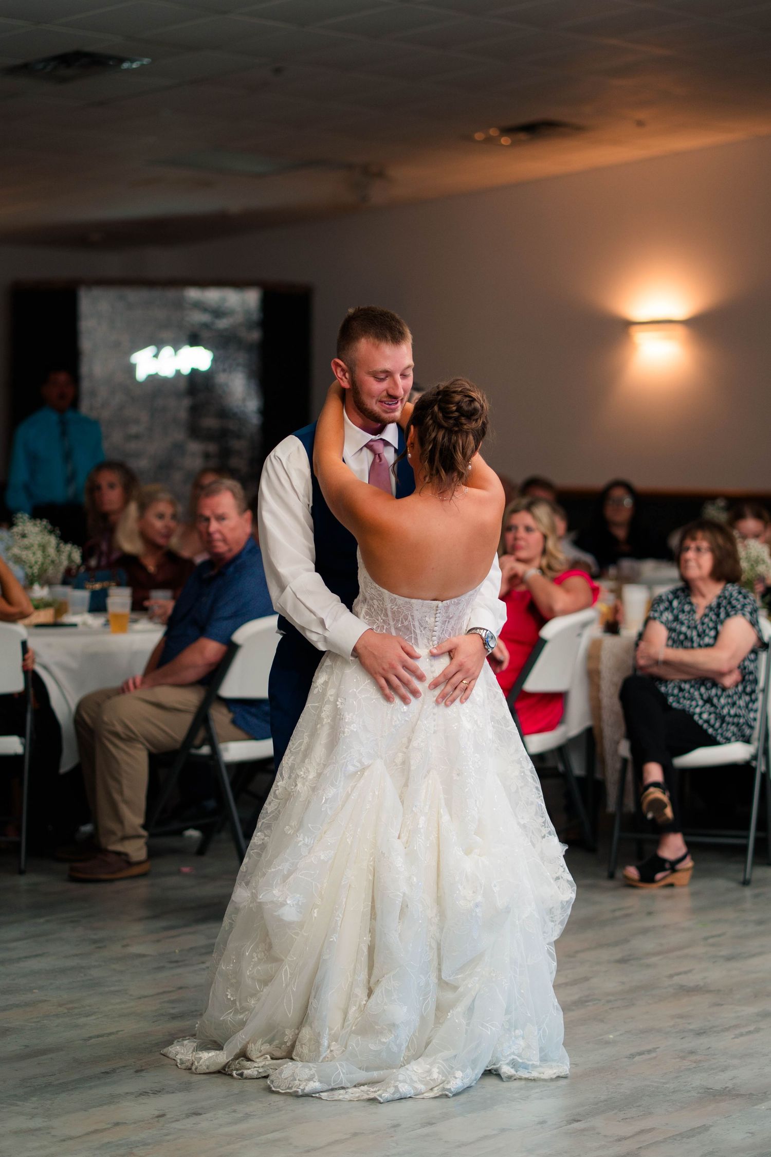 Newlyweds share their first dance as wedding guests watch from surrounding tables at the reception.