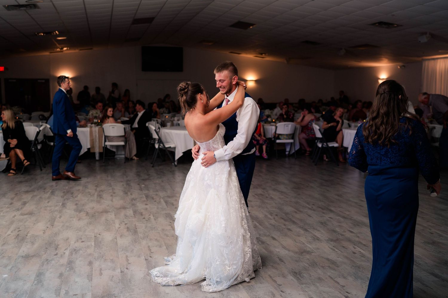 Bride and groom share their first dance together in the center of the reception hall surrounded by seated guests.