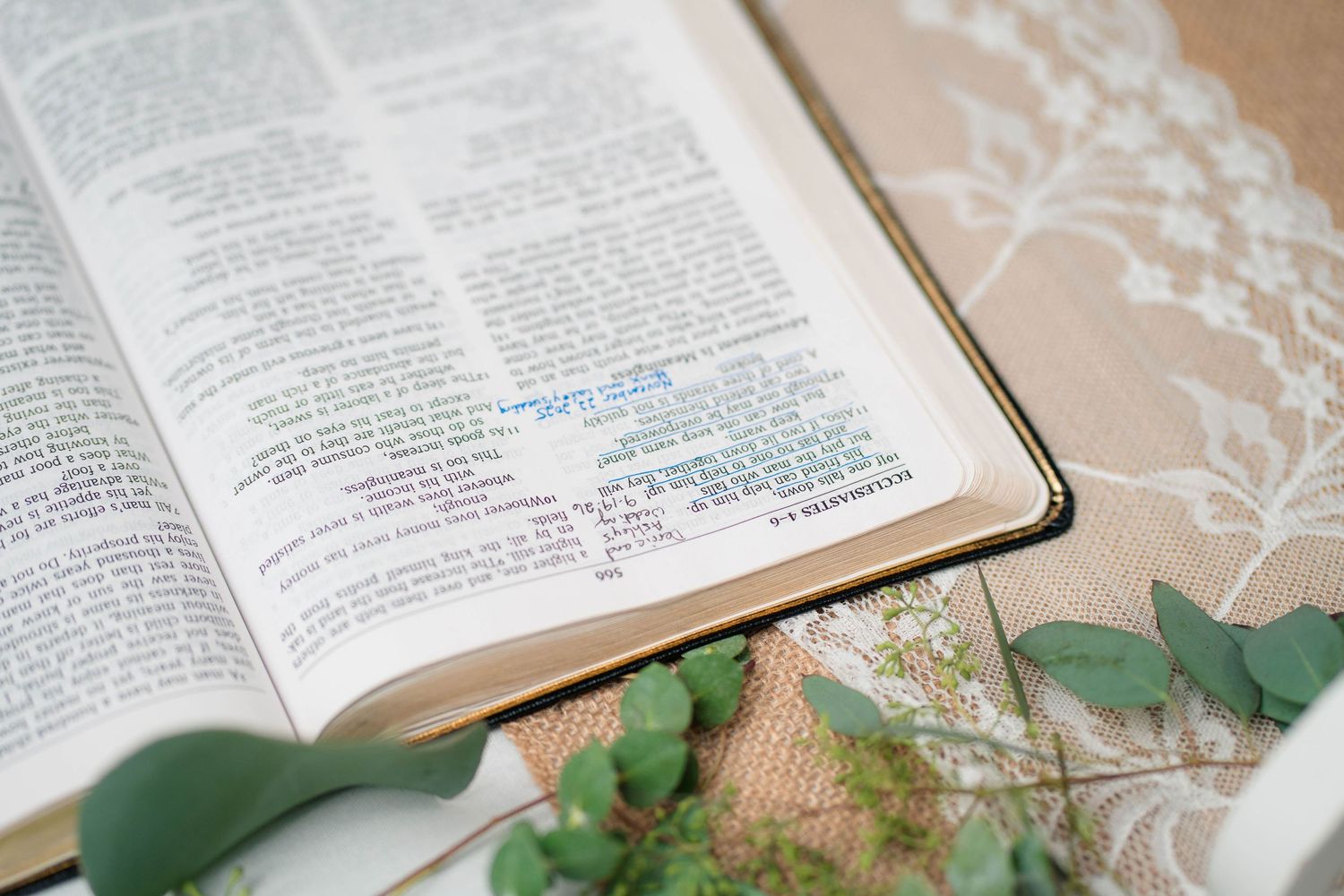 Open Bible with highlighted verses displayed with eucalyptus and white lace at wedding.