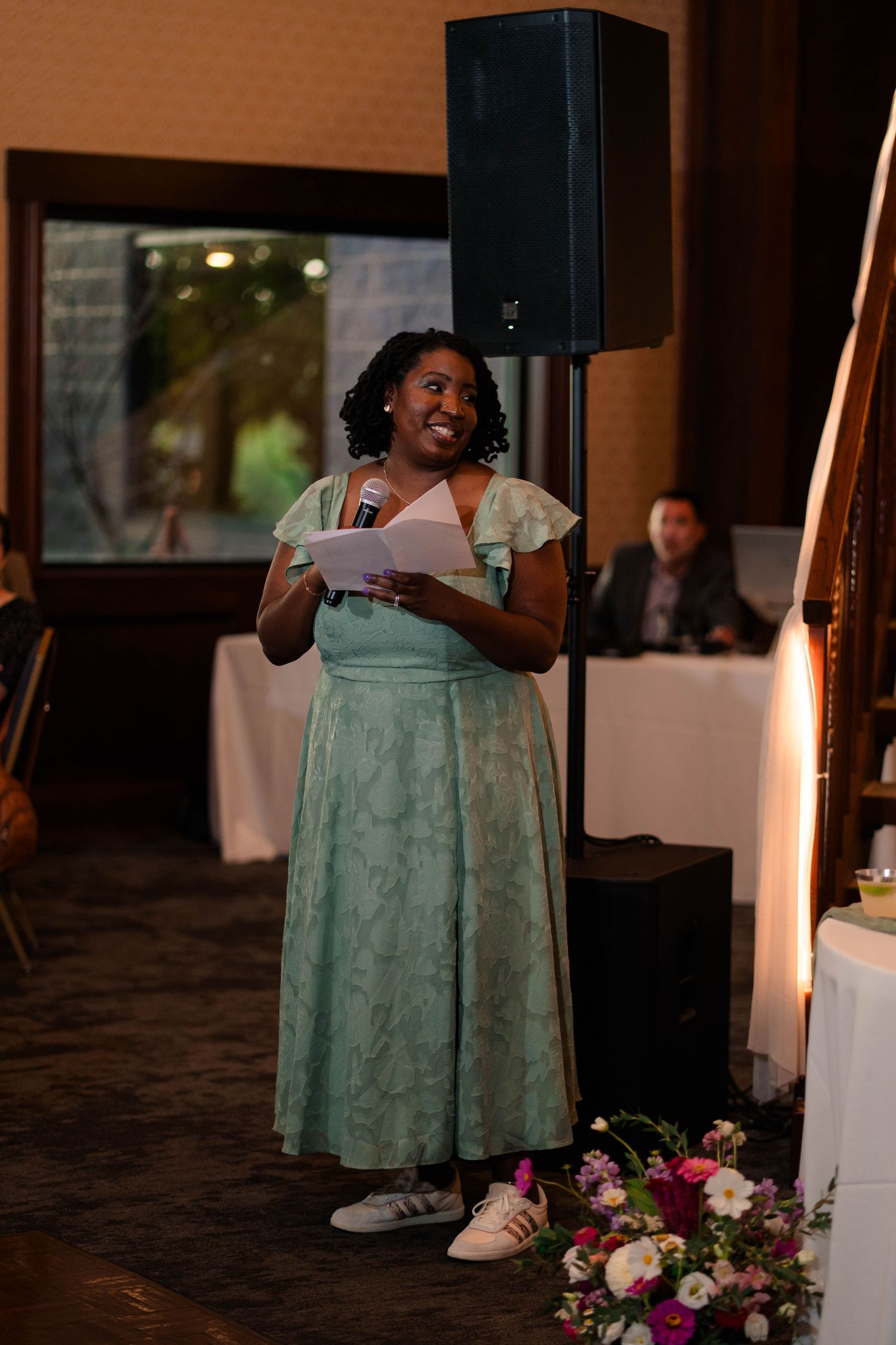 Woman in mint green dress smiling while delivering a speech at a wedding reception.