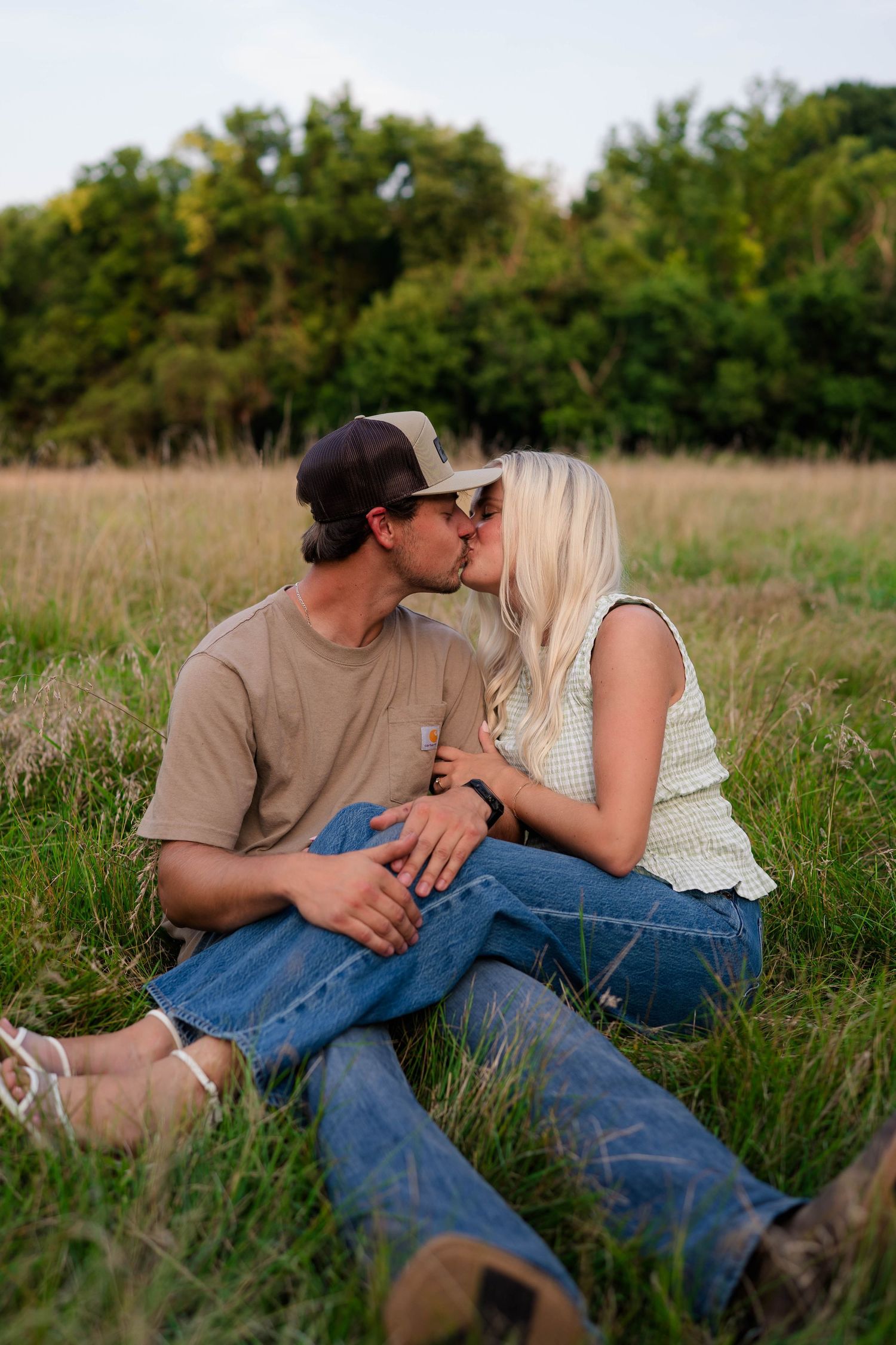 Couple sharing a kiss while sitting together in a lush green meadow on a sunny day.