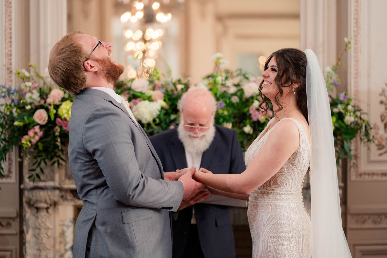 Bride and groom exchange vows at elegant floral altar with officiant during indoor wedding ceremony.