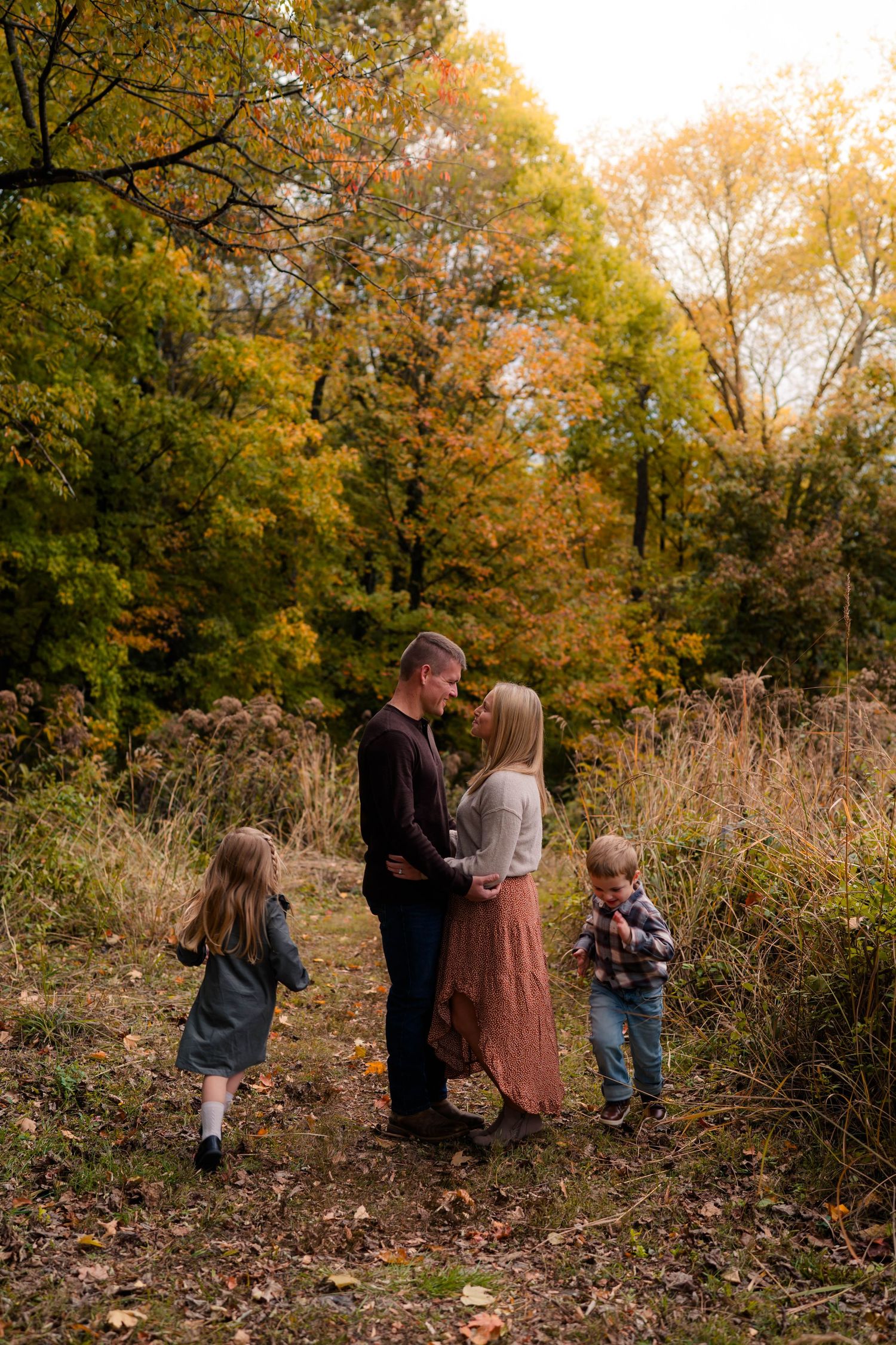 Family of four shares a tender moment on an autumn forest path with golden foliage.