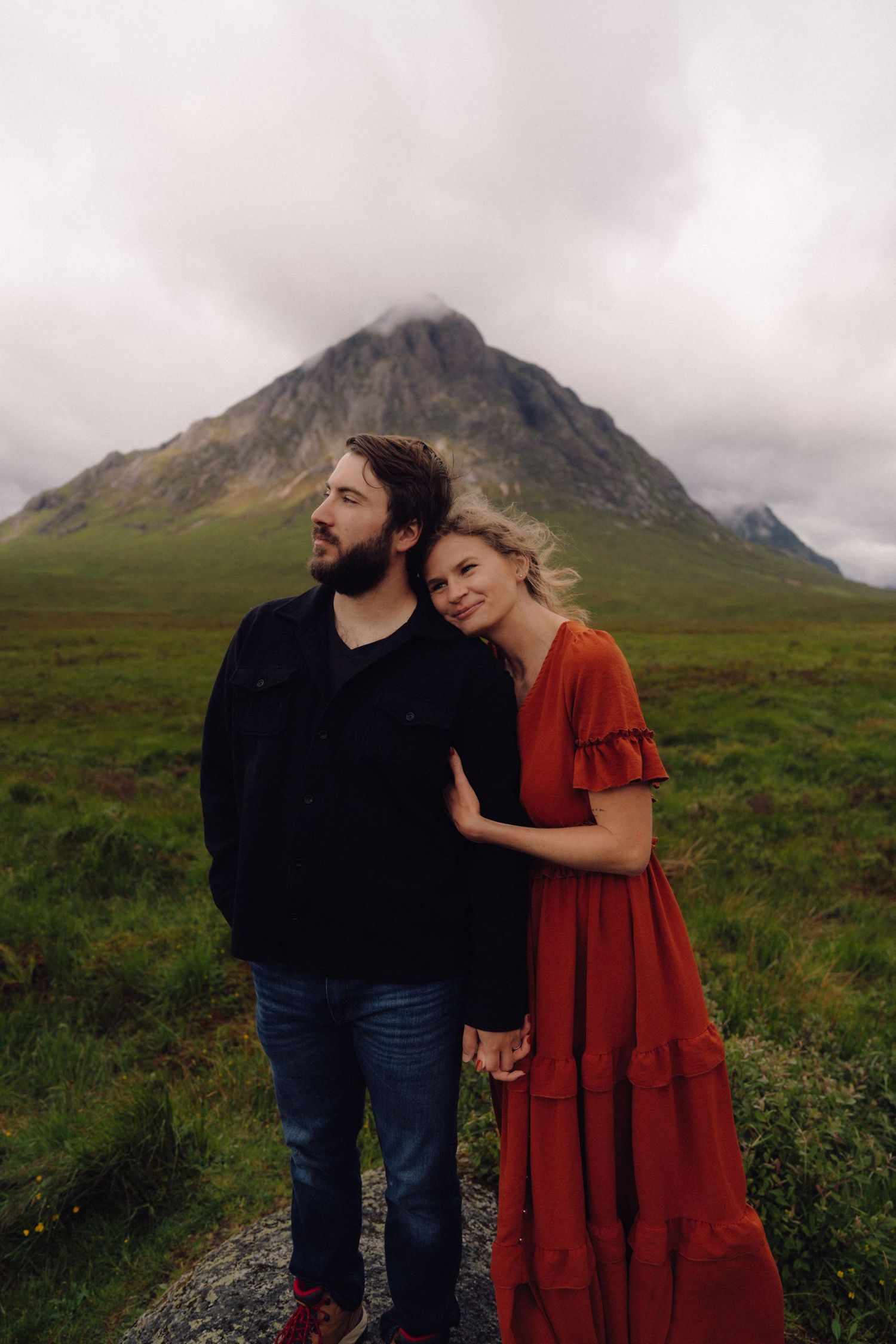 Couple holding hands before misty mountain in Scottish Highlands landscape.