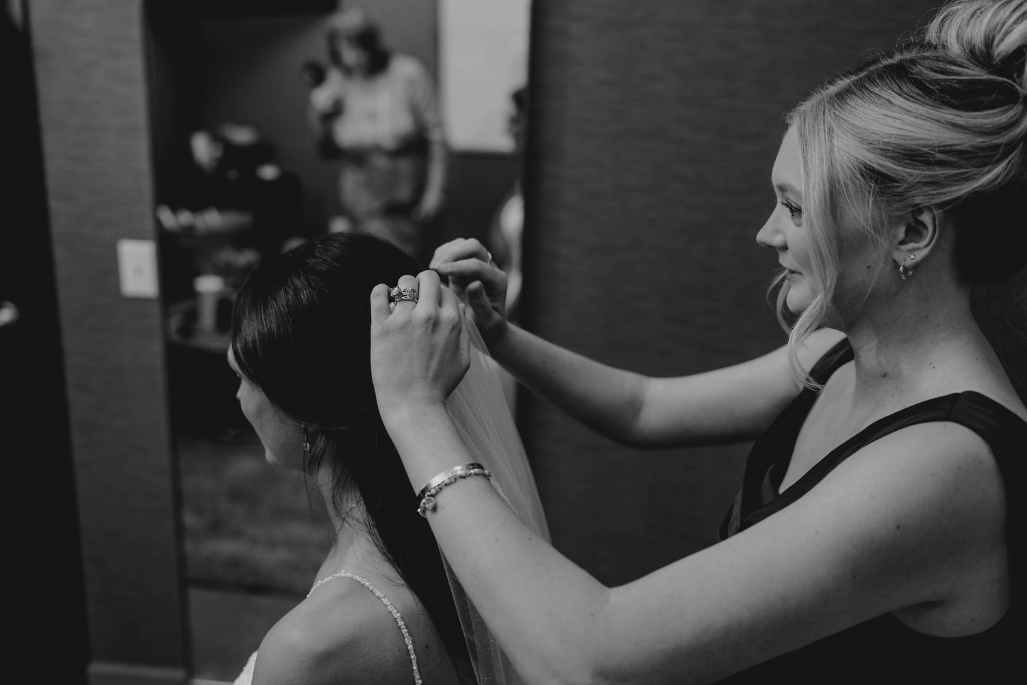 Black and white photo of a hairstylist styling the brides hair before the wedding ceremony.