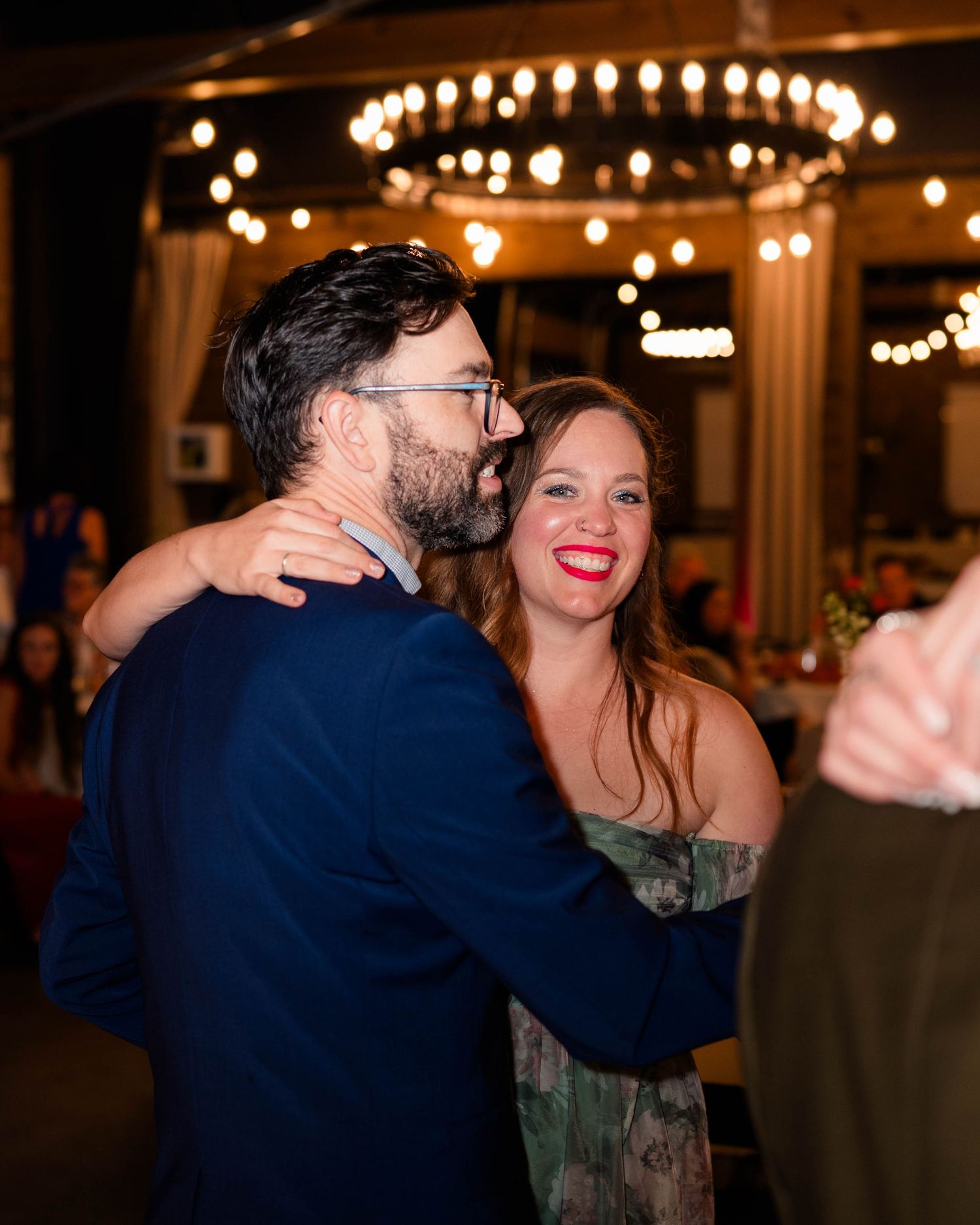 Couple shares a romantic dance under chandelier string lights at elegant wedding reception.