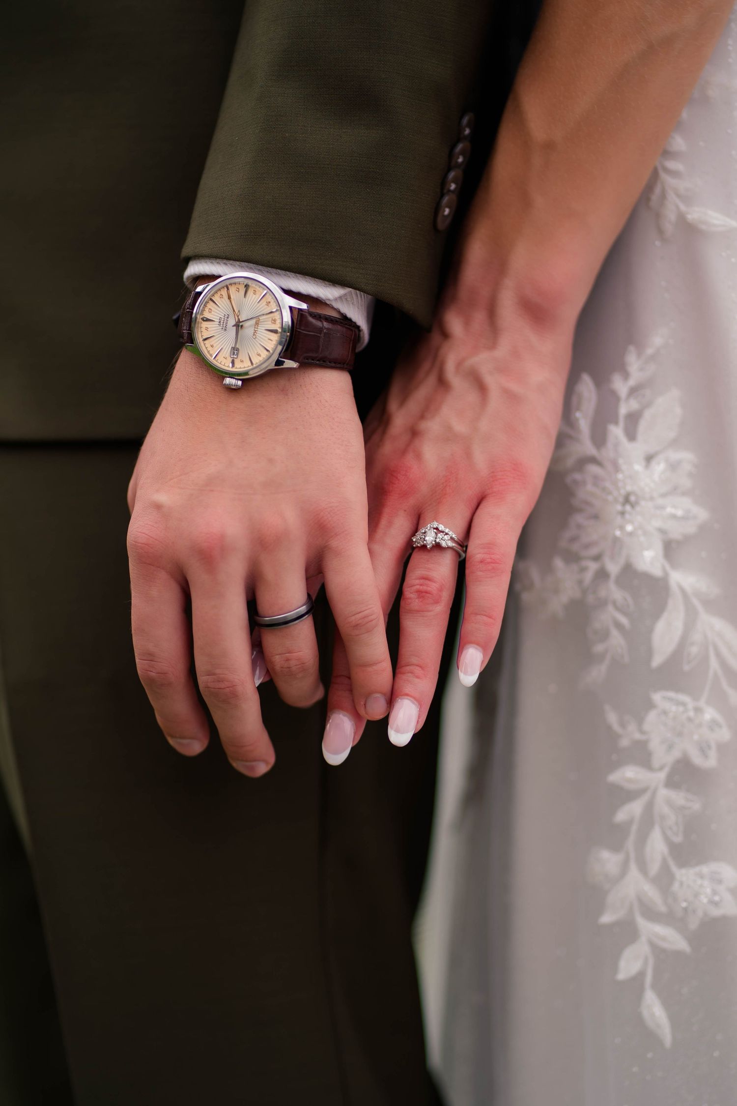 Close-up of bride and groom showing off wedding rings, groom wearing a classic brown leather strap watch.