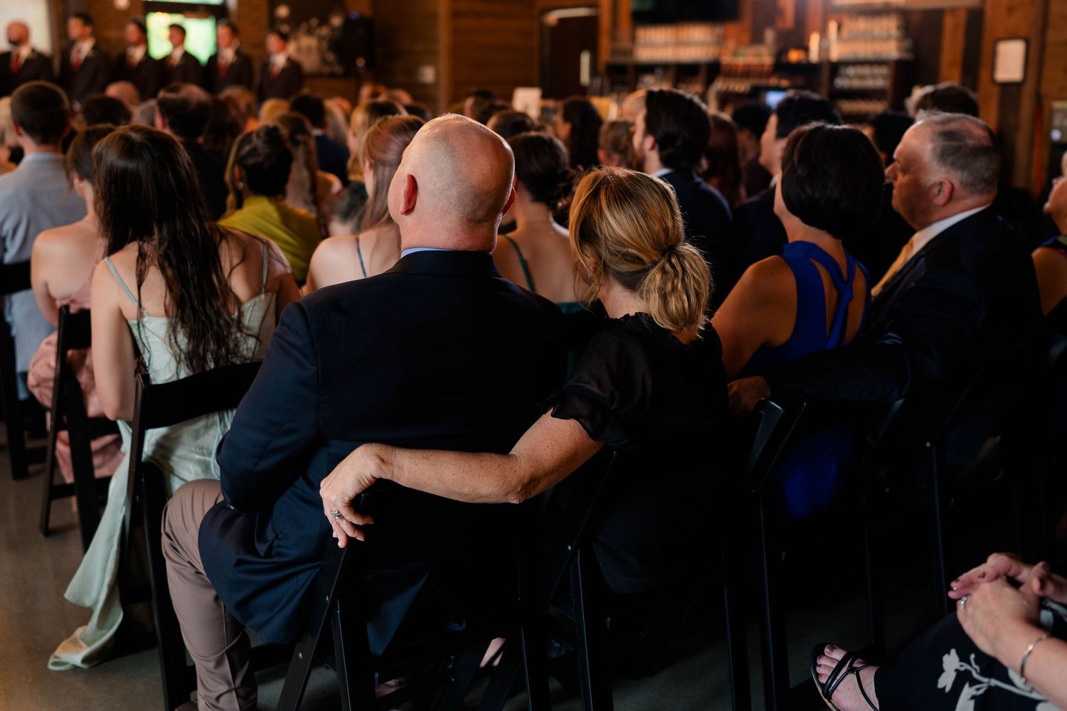 Wedding guests seated together watching ceremony in warmly lit rustic venue.