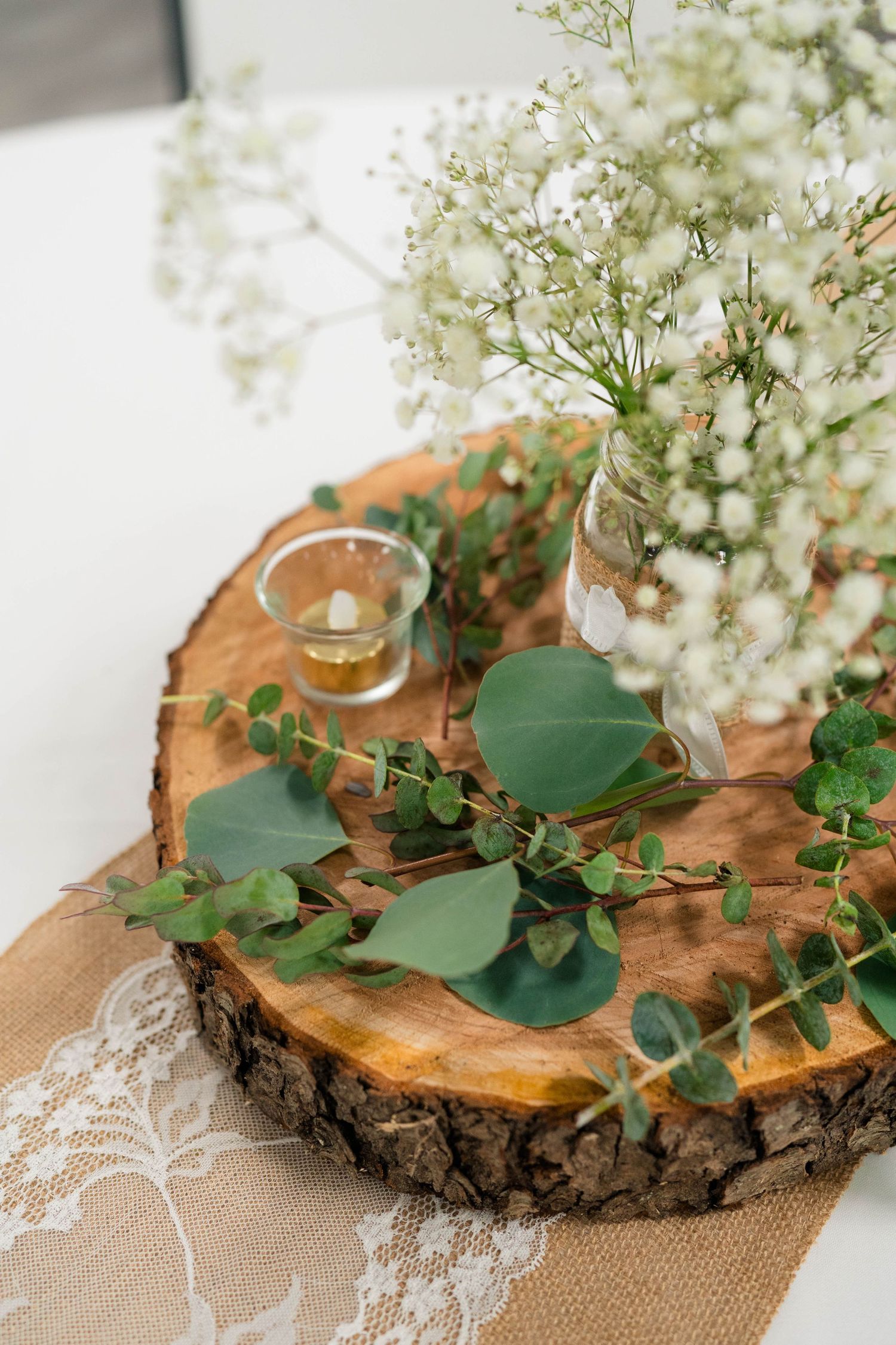 Close-up of rustic wedding centerpiece featuring baby's breath, eucalyptus, and a candle on wood slice.