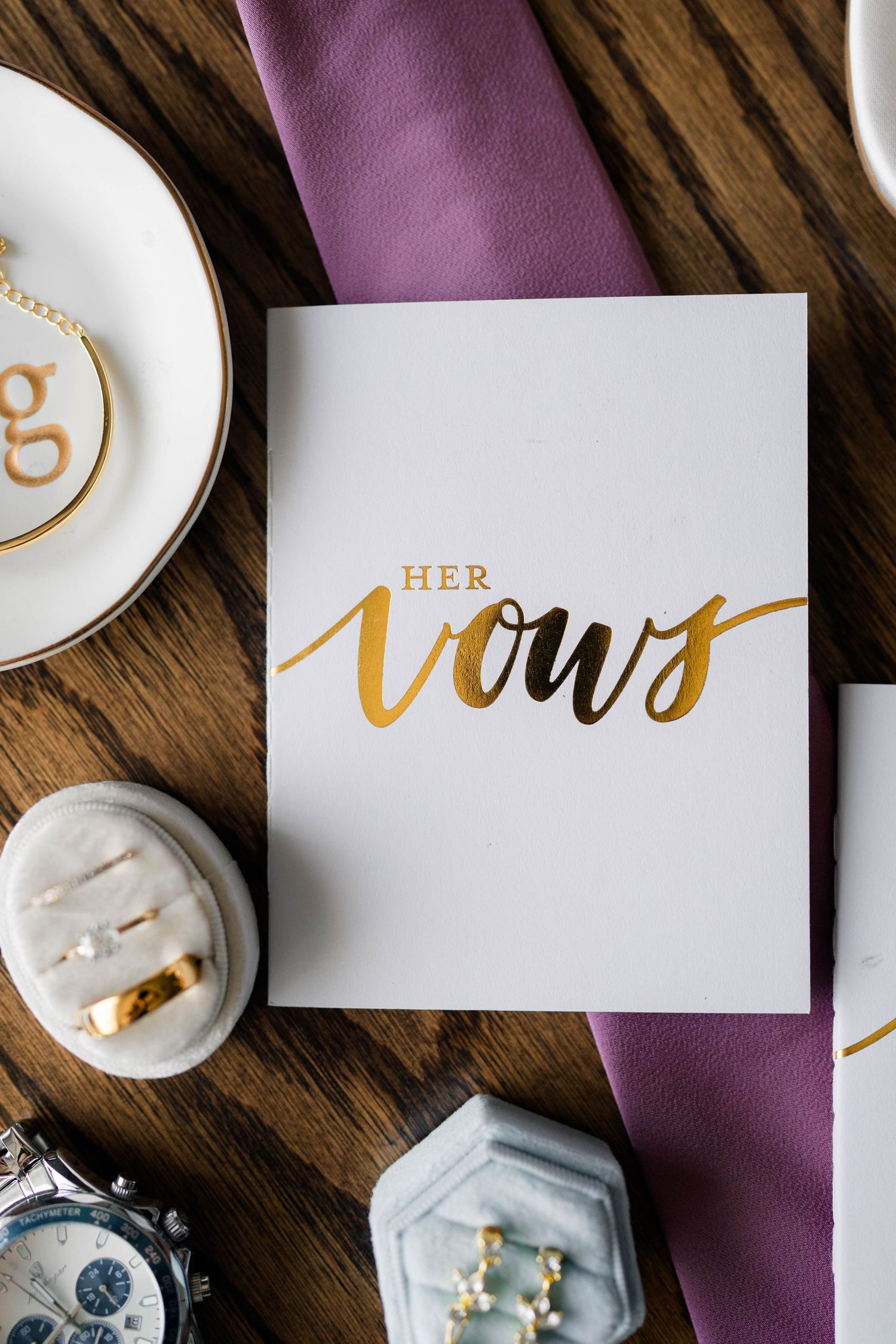 Close-up of elegant white and gold foil Her Vows wedding booklet on wooden surface with accessories.
