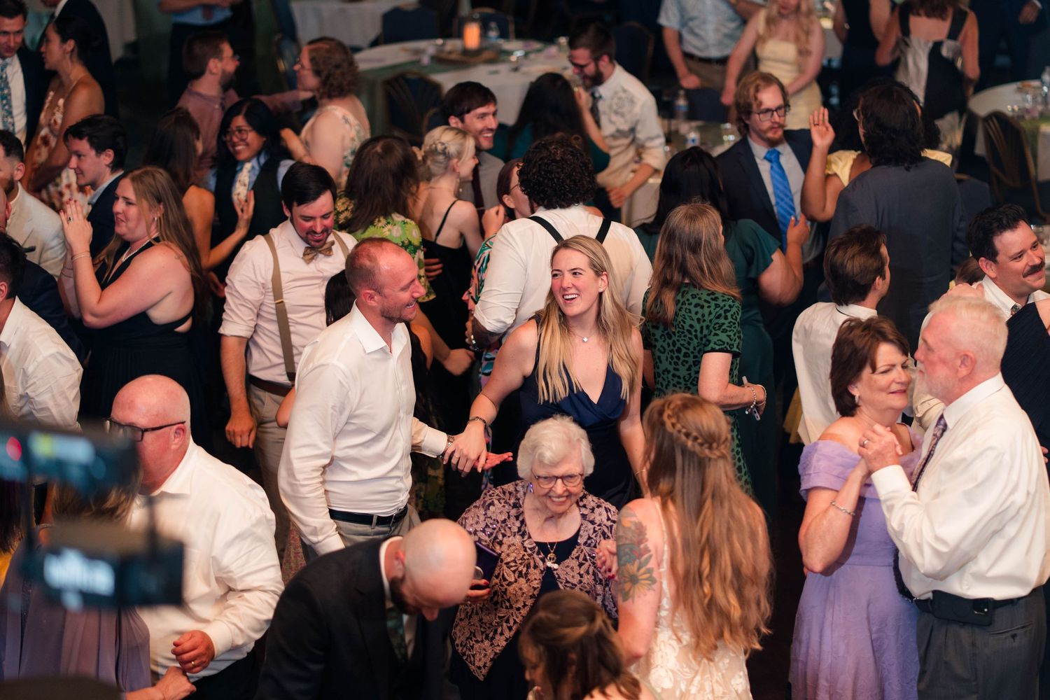 Guests celebrate and dance together at a lively wedding reception in a bright event venue.