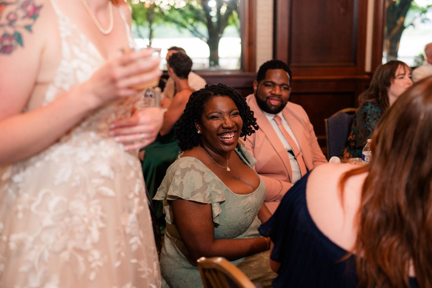 Joyful wedding guests laugh and smile during a lively indoor wedding reception celebration.