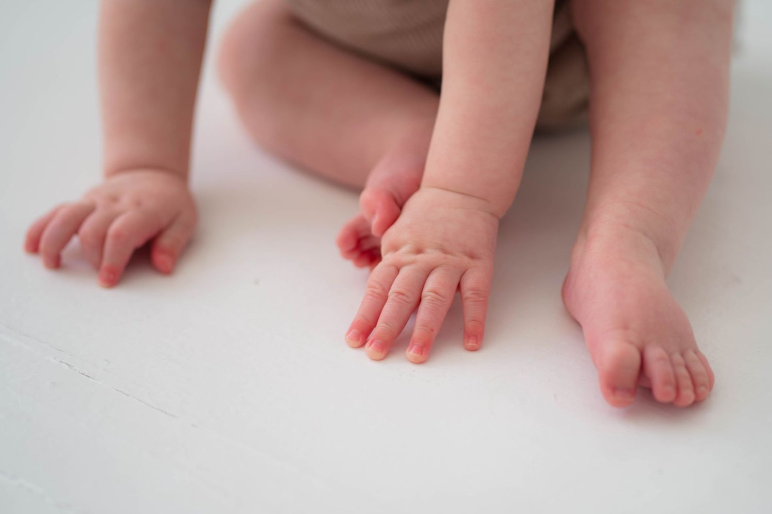 Close-up of cute baby hands and feet on a white surface, newborn detail photo.