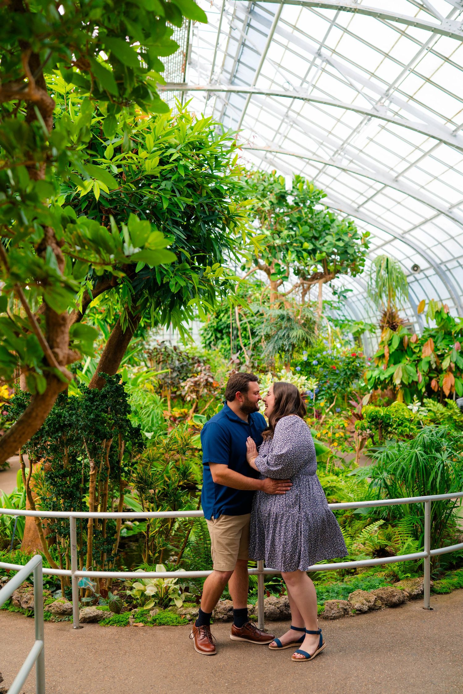 Couple sharing a kiss on a path inside a lush tropical greenhouse conservatory.