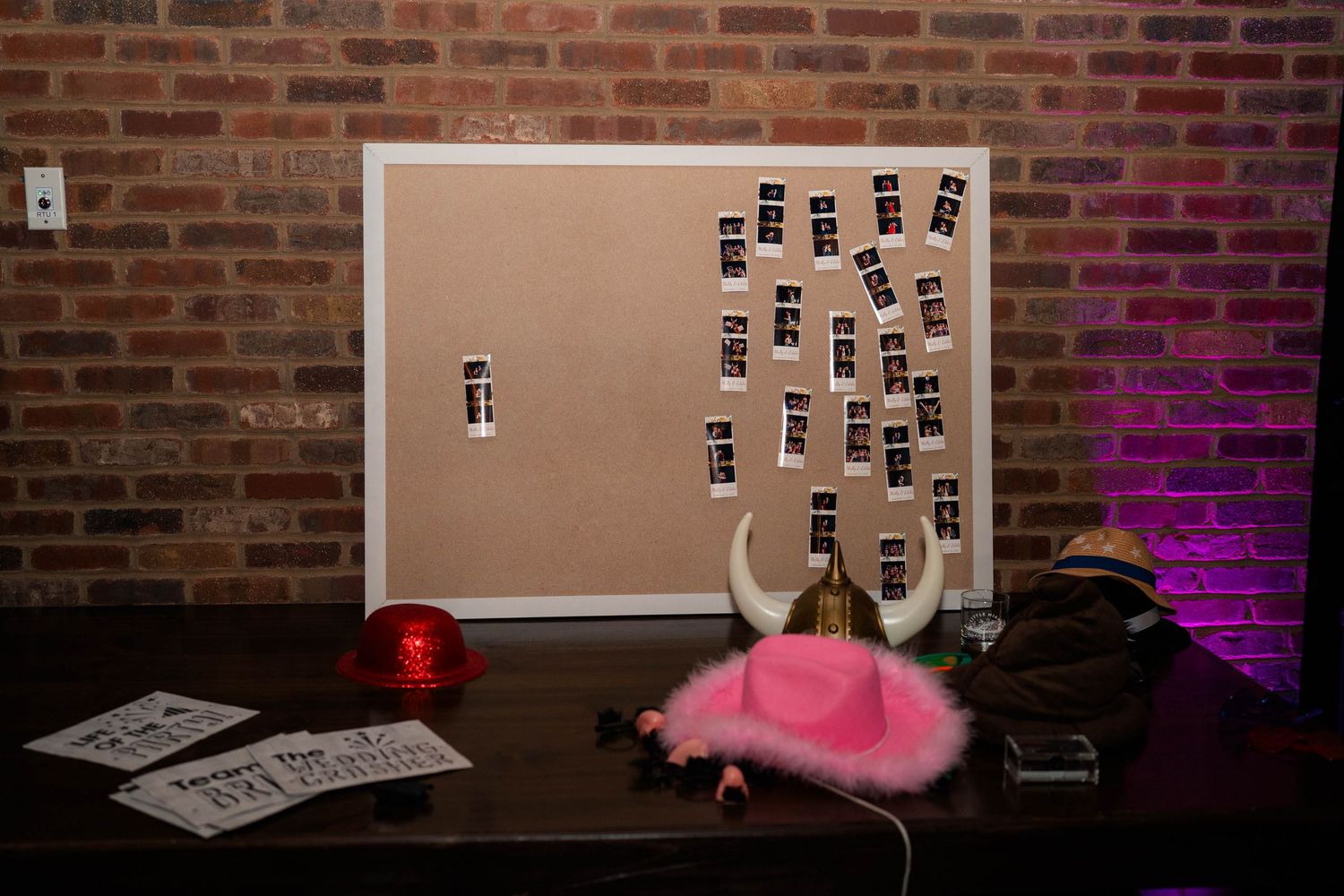Wedding photo booth display board with Polaroid photos and fun props including pink cowboy hat on table.
