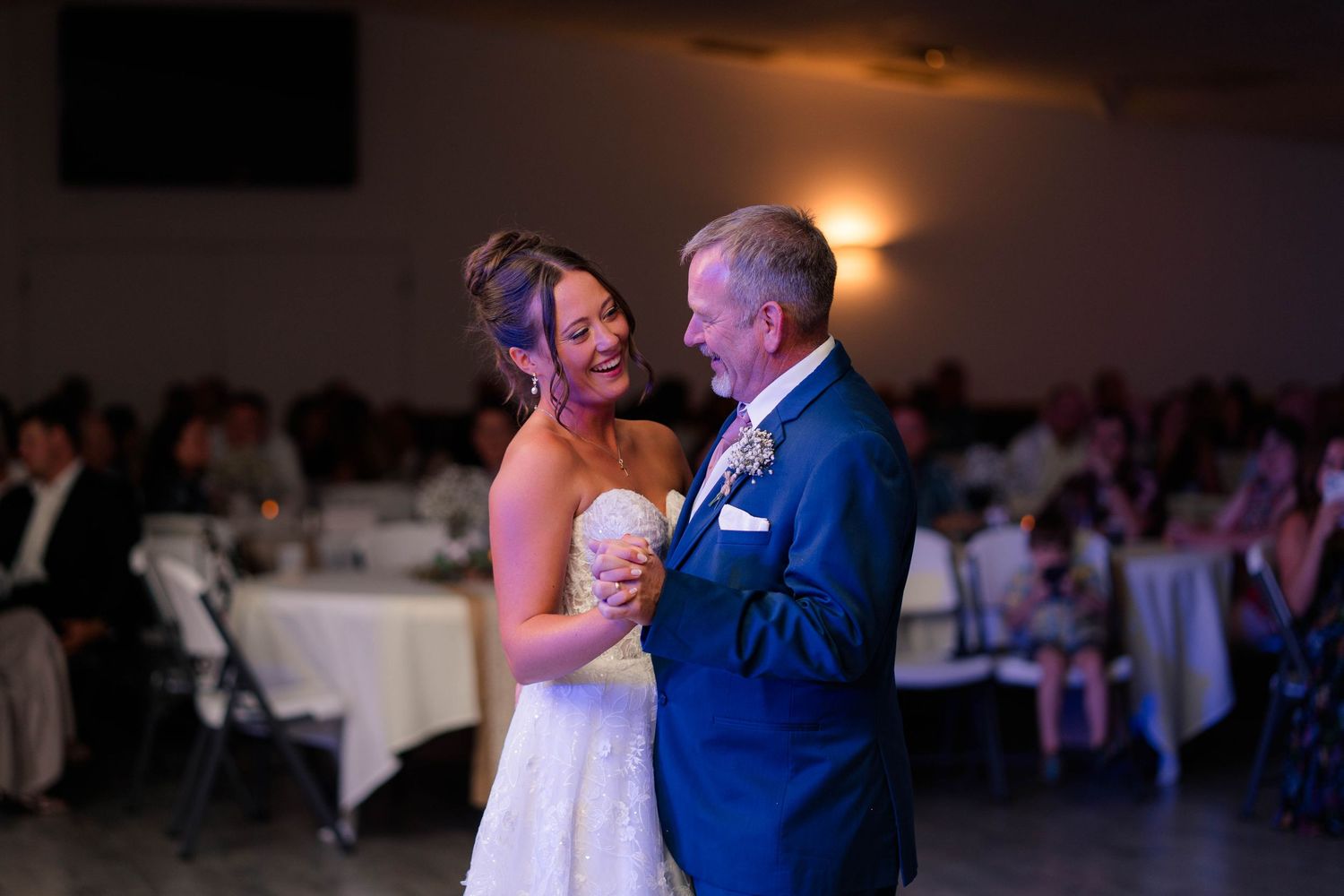 Bride shares joyful father-daughter dance at wedding reception in elegant venue.