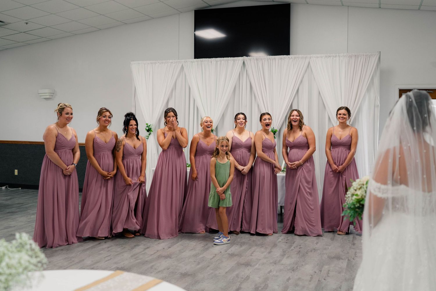Bridesmaids in dusty rose gowns with flower girl in green dress standing at wedding ceremony altar.
