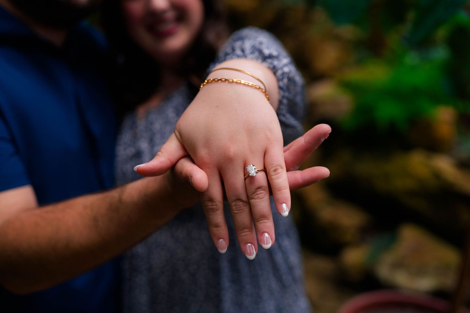 Close-up of an engagement ring on womans hand held by her fiance in a garden setting.