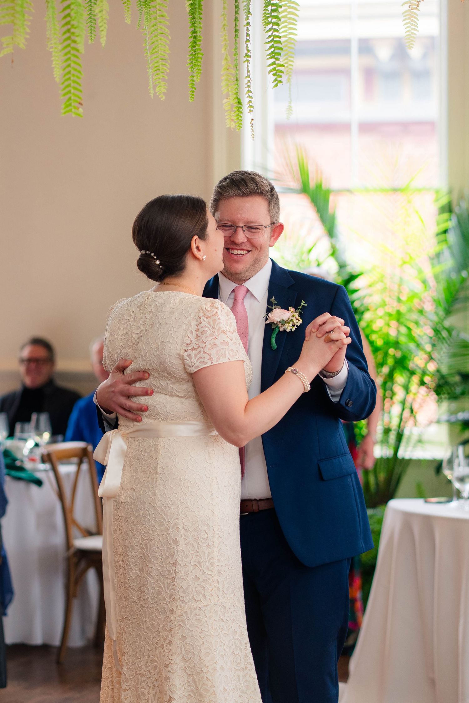 Bride and groom sharing first dance in lace dress and navy suit at botanical wedding.