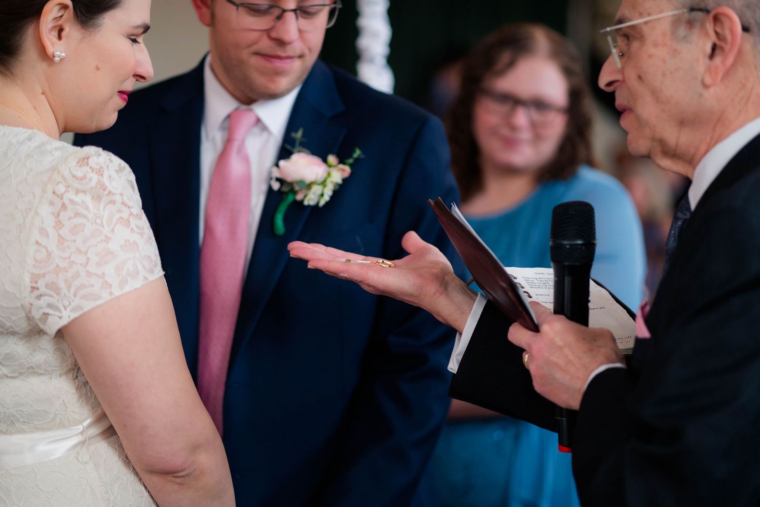 Officiant gestures over open book during intimate wedding ring exchange ceremony.