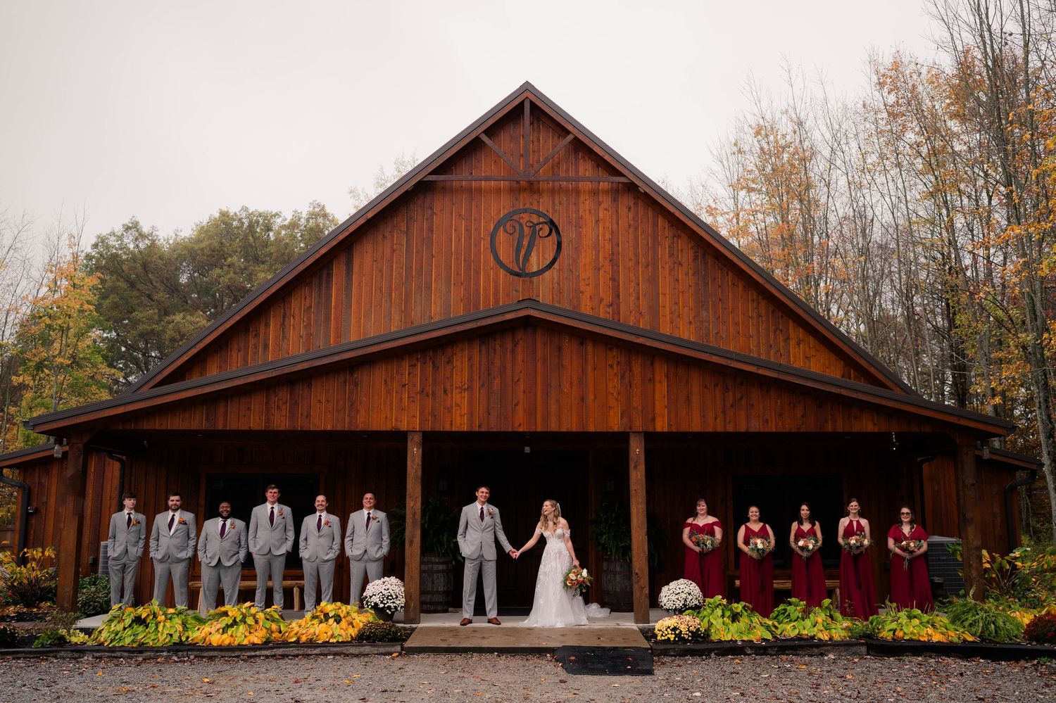 Wedding party poses on rustic barn venue porch with groomsmen and bridesmaids in burgundy dresses.