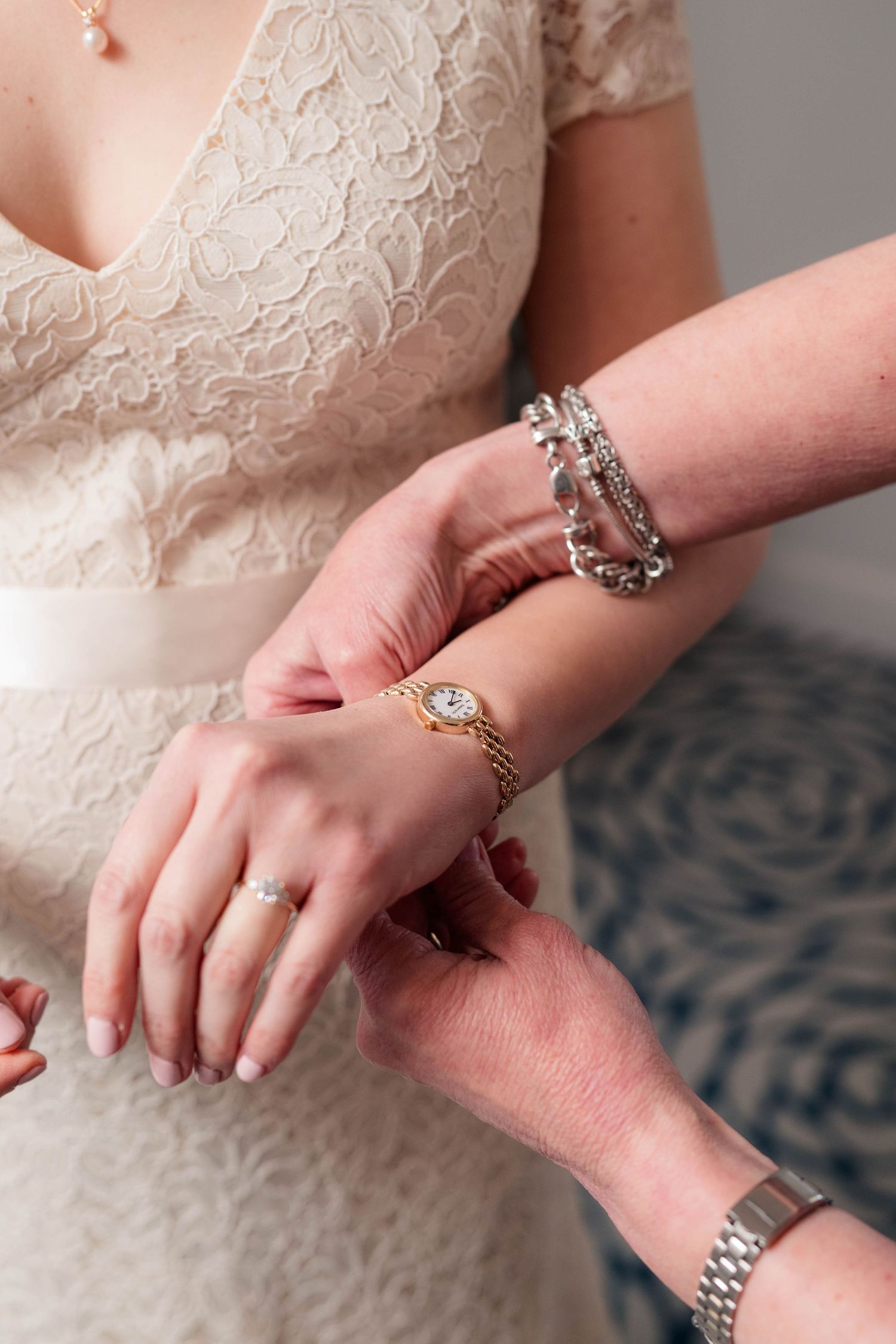Close-up of bride's hands adorned with diamond ring and silver bracelet on lace dress.