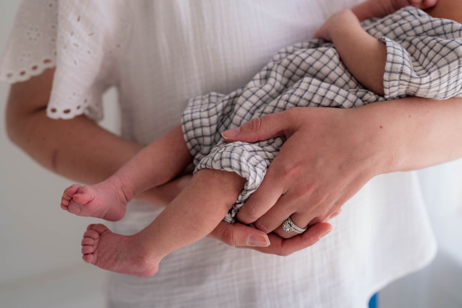 Close-up of a mother holding her newborn baby, showcasing tiny feet and delicate fingers in soft natural light.