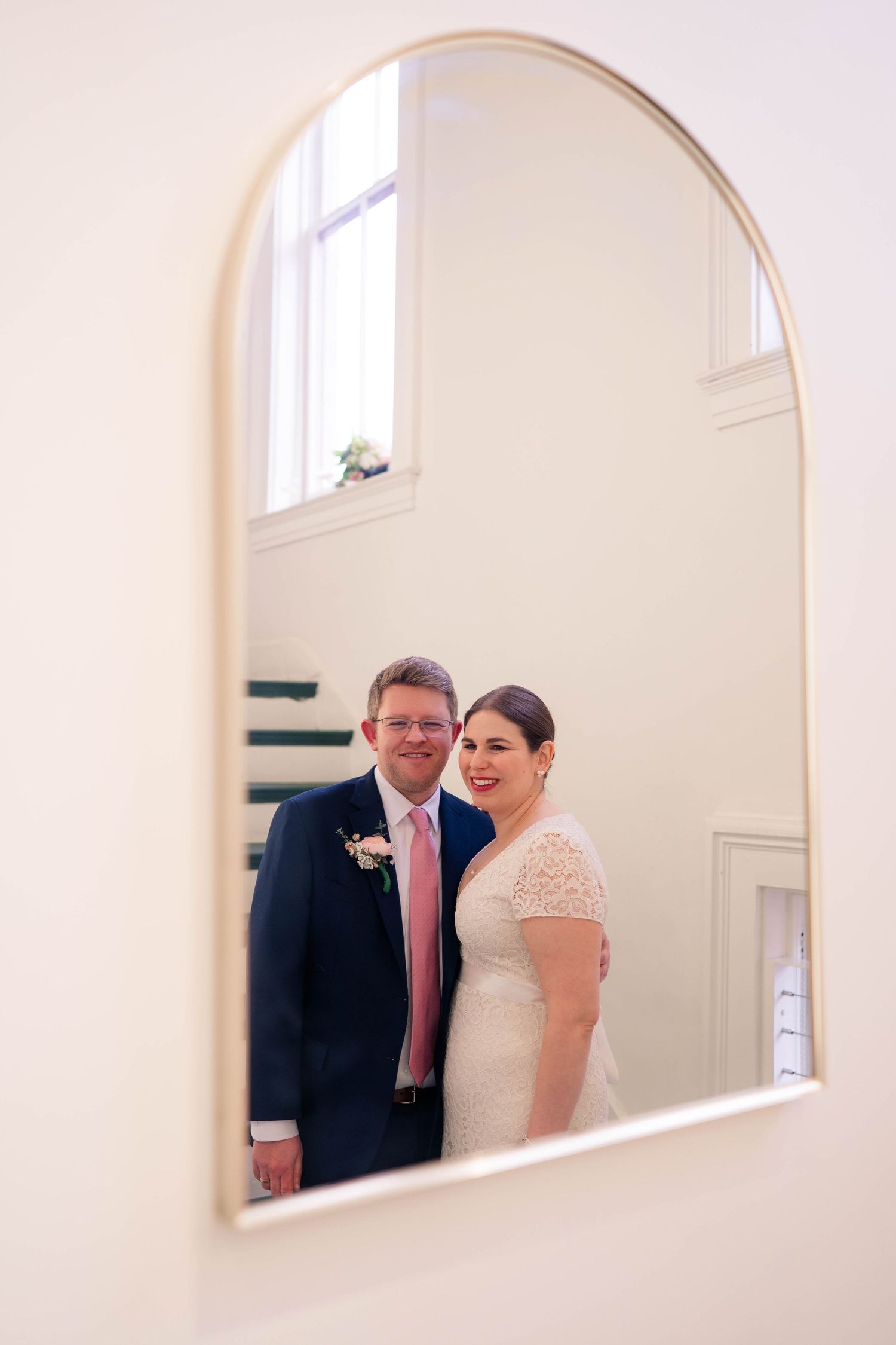 Bride and groom smiling together reflected in an arched gold mirror.