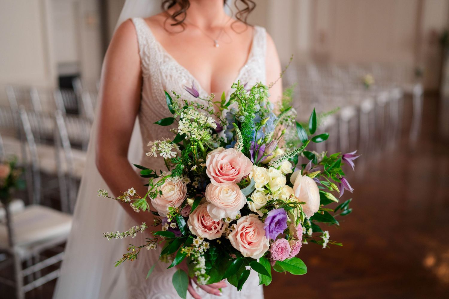 Bride holding a lush wedding bouquet with pink roses, purple flowers, and greenery.