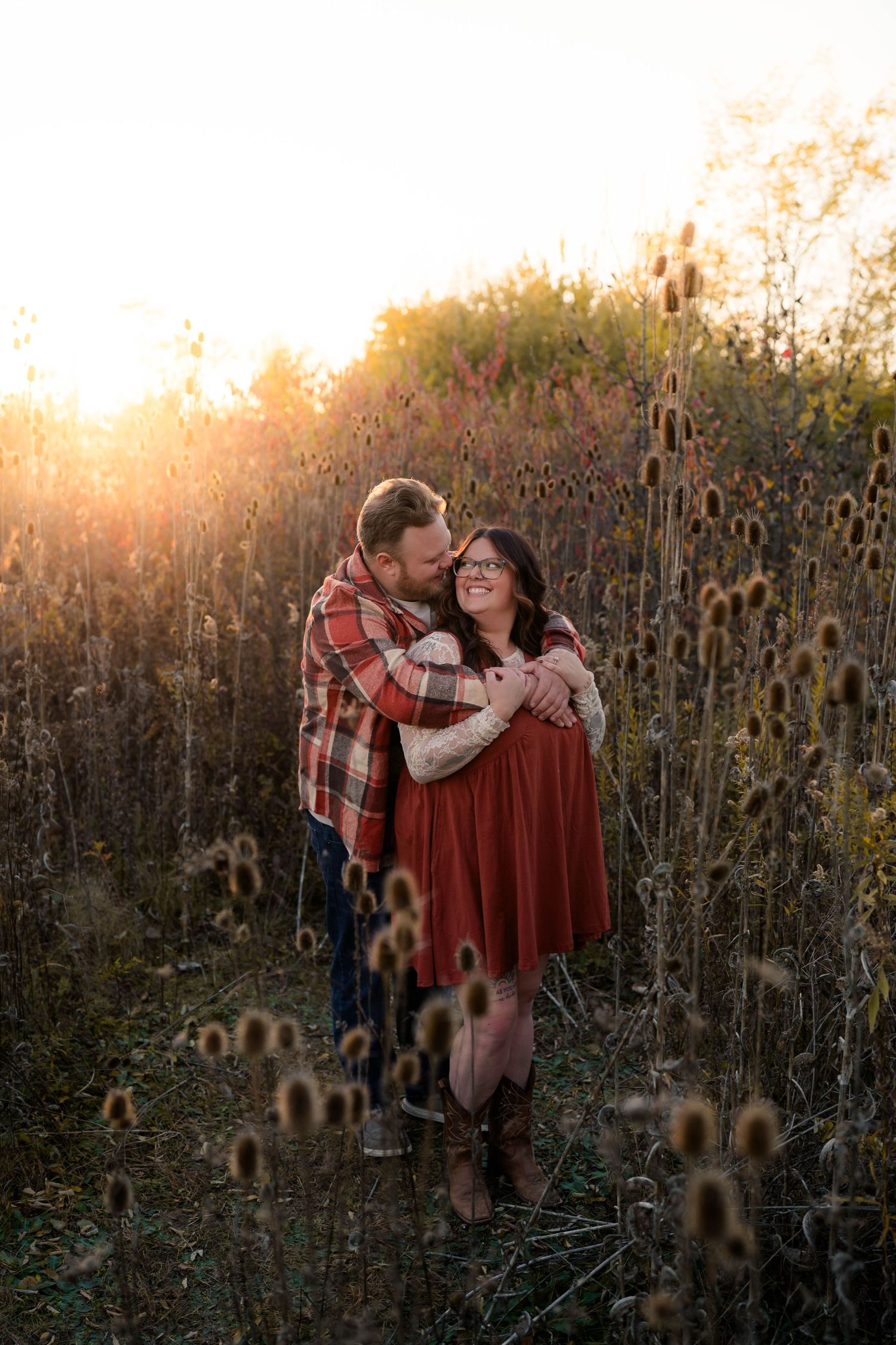 Couple embracing in a golden sunlit field of wildflowers during autumn engagement photo session.