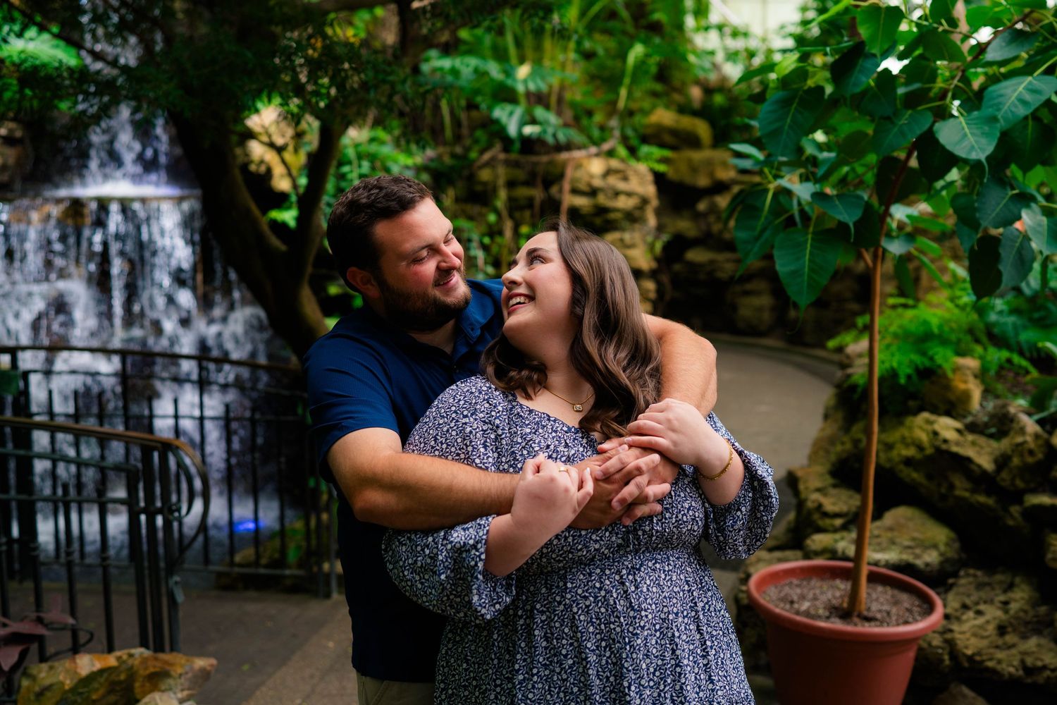 Couple dancing and laughing together in a lush garden with a waterfall backdrop during their engagement session.