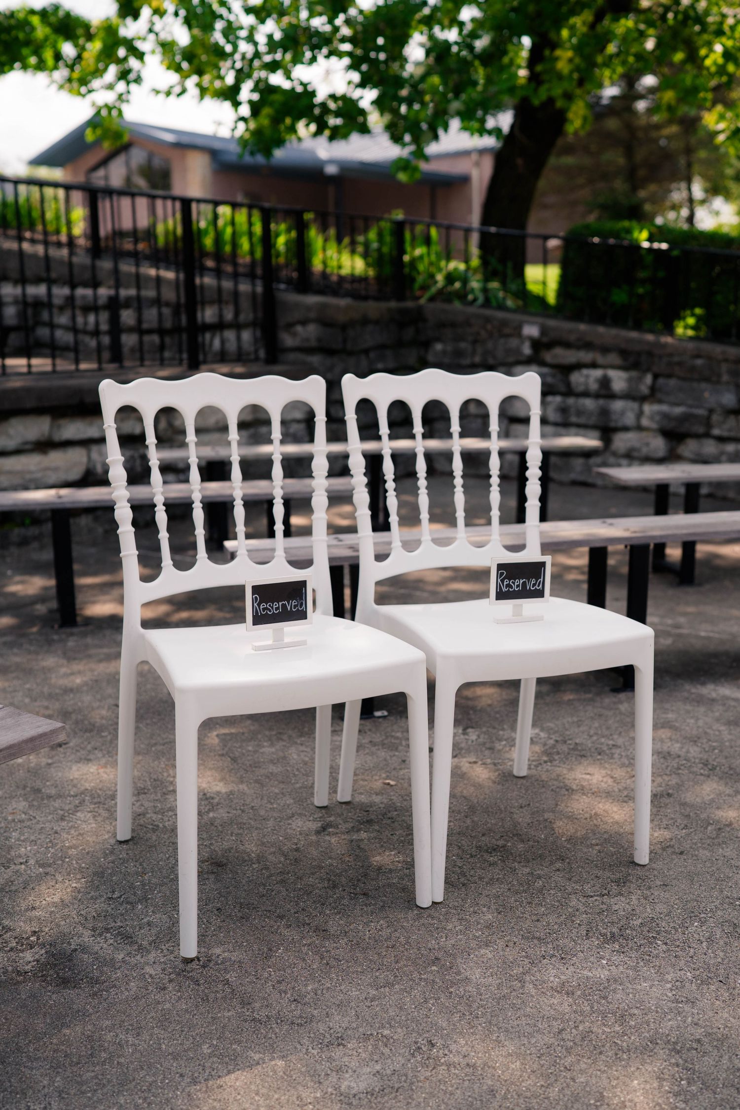 Two white ornate reserved chairs with chalkboard signs at an outdoor wedding ceremony venue.