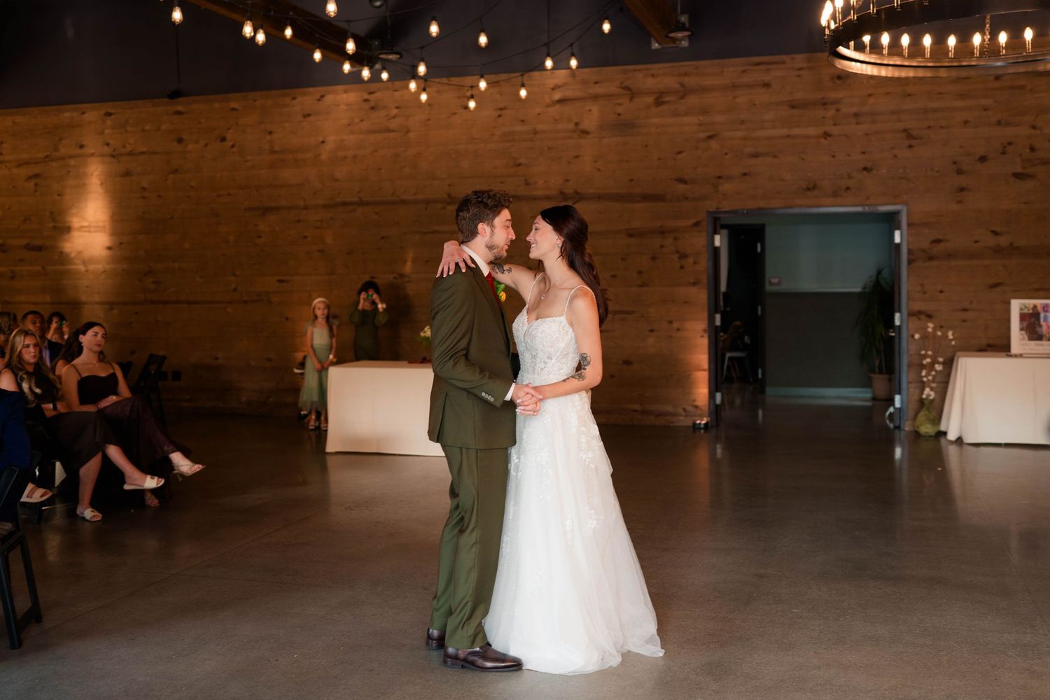 Bride and groom share intimate first dance in warmly lit industrial wedding venue.