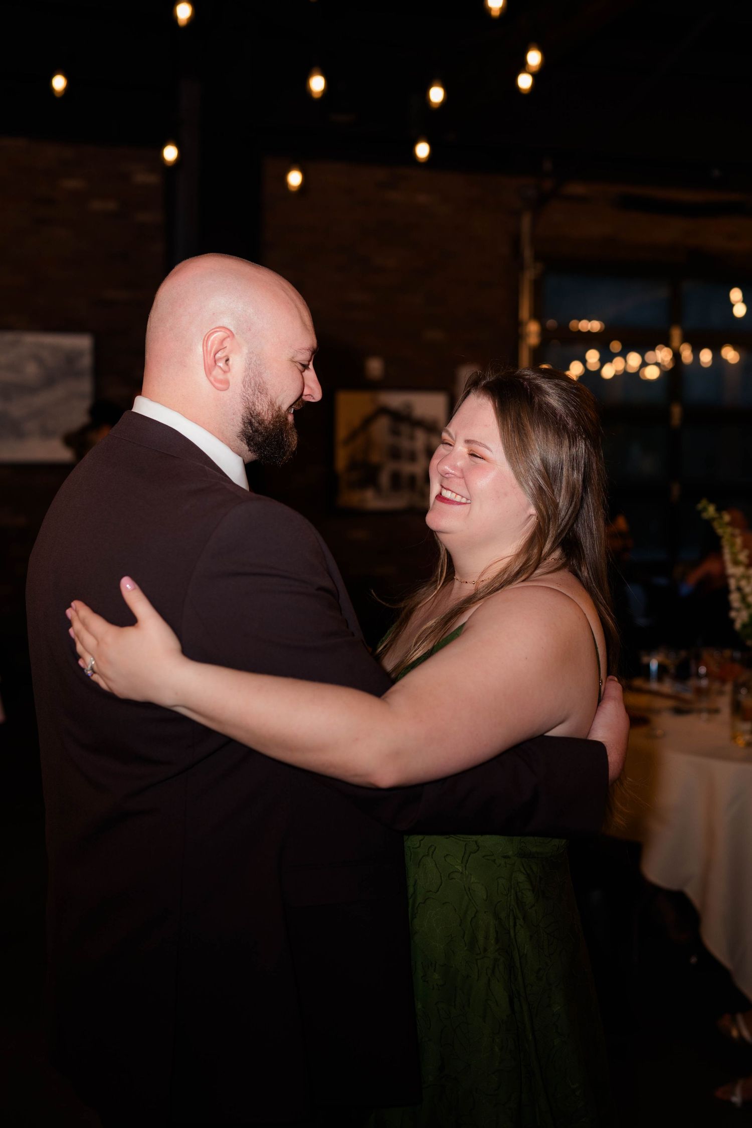 Couple in formal attire share a laugh while dancing at a wedding reception.