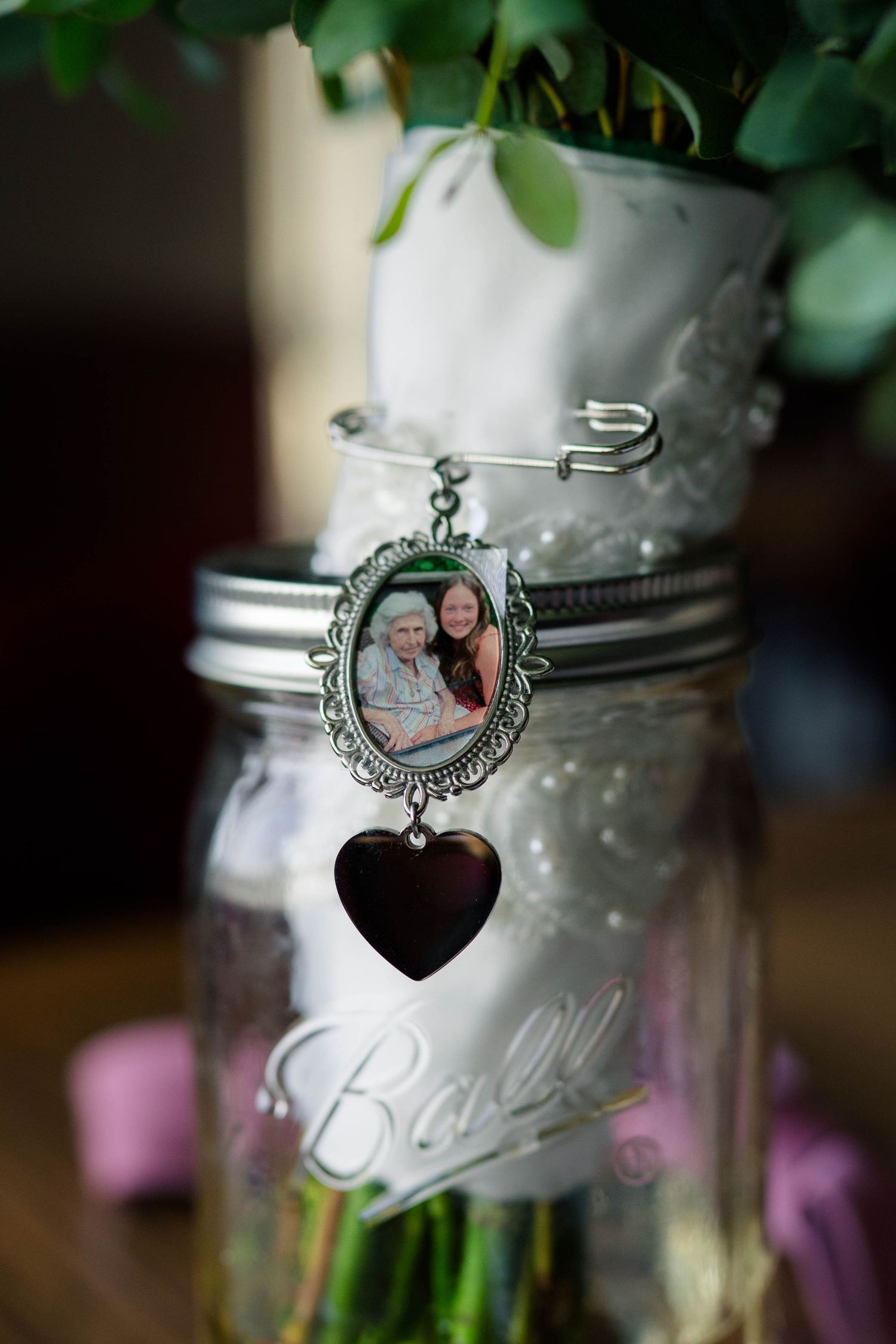A memorial photo charm with a heart pendant pinned to a white ribbon on a Ball mason jar wedding bouquet.