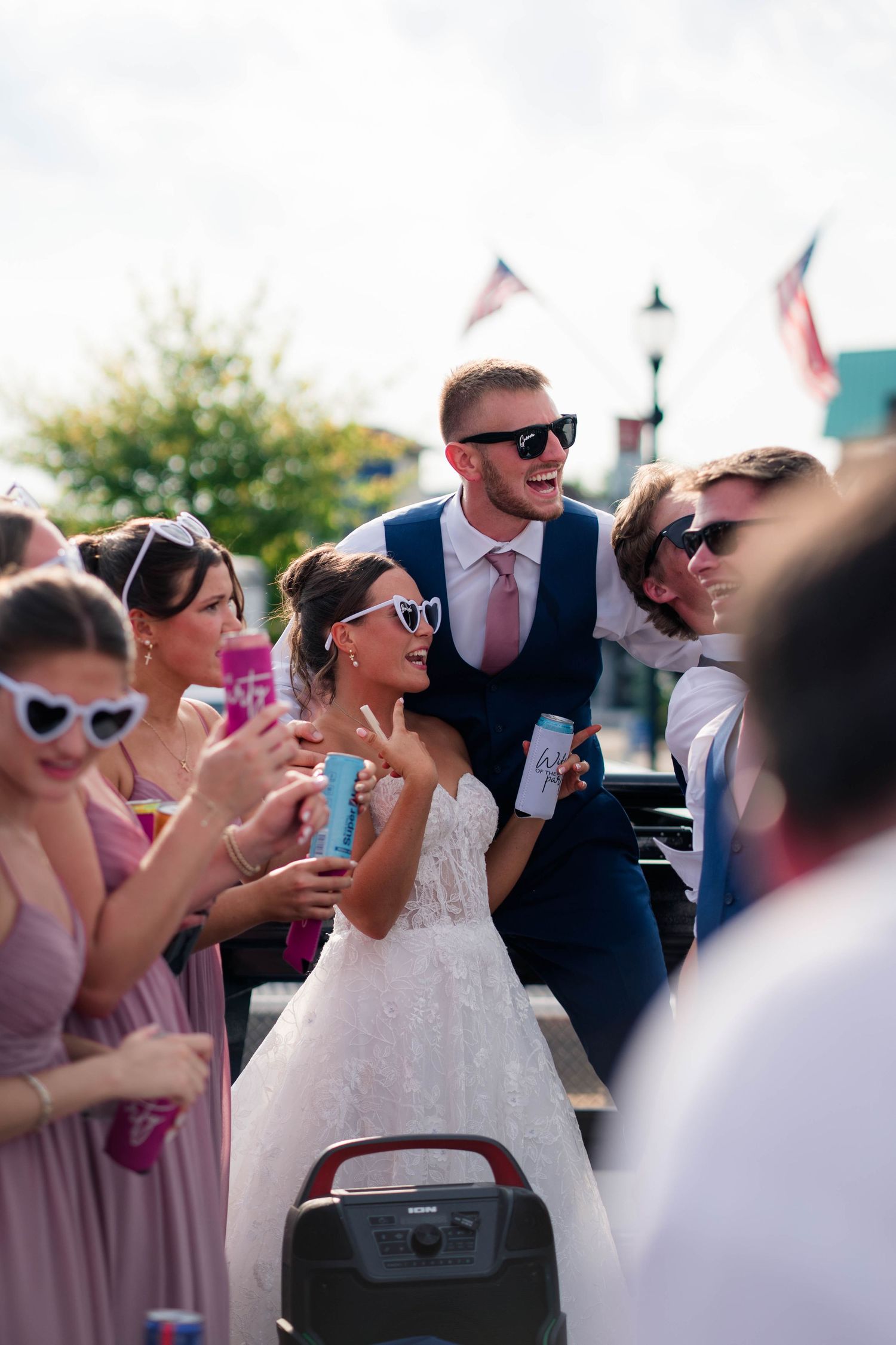 Bride and groom celebrating with guests on a flatbed truck at an outdoor wedding reception.