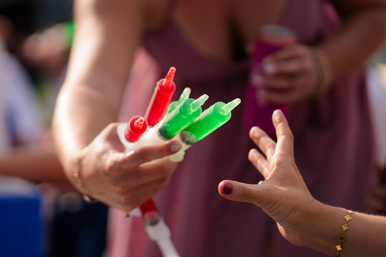 Adult hands pass colorful popsicles to a child's outstretched hands at a summer wedding reception.