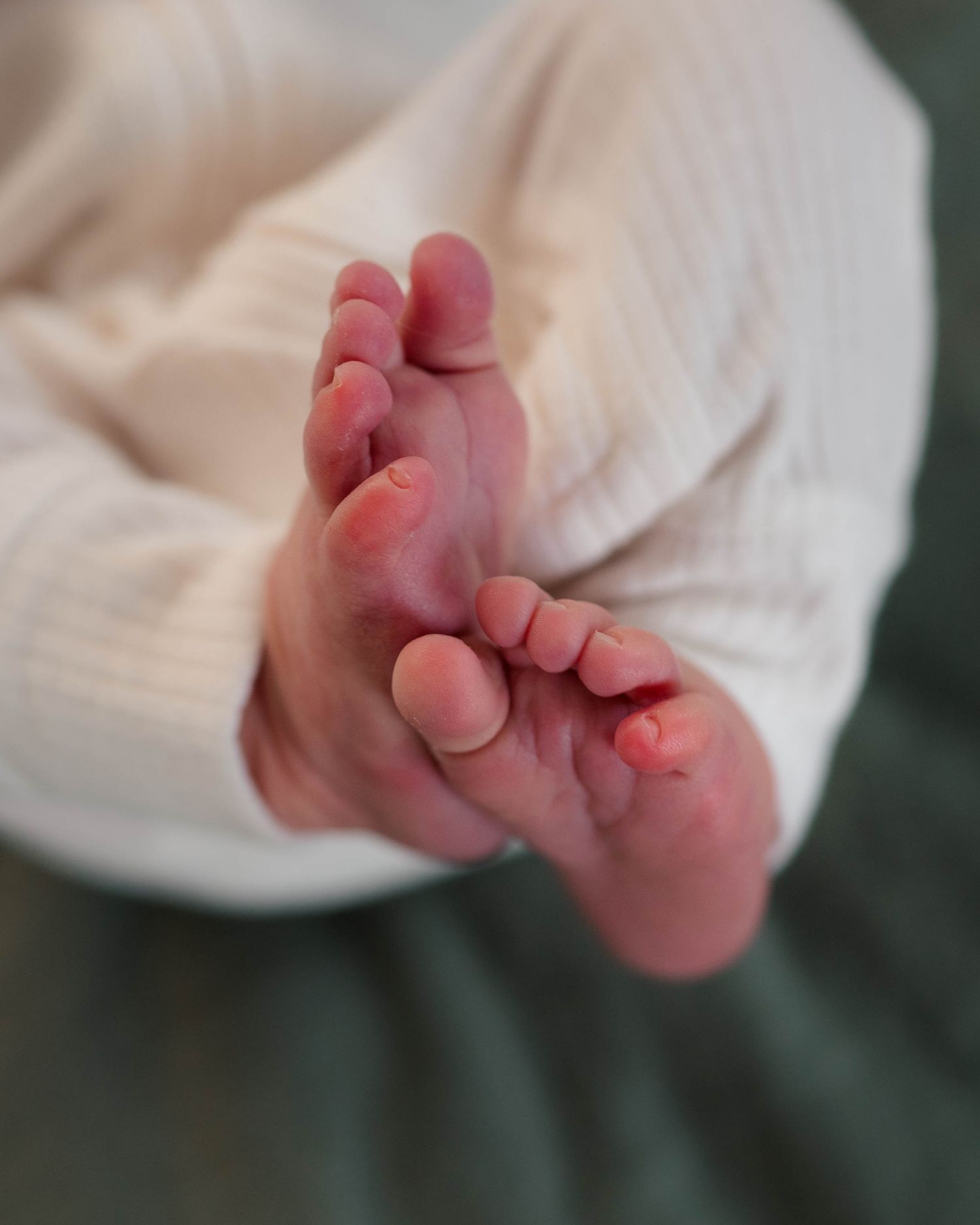 Close-up of tiny newborn baby feet crossed in white ribbed outfit.