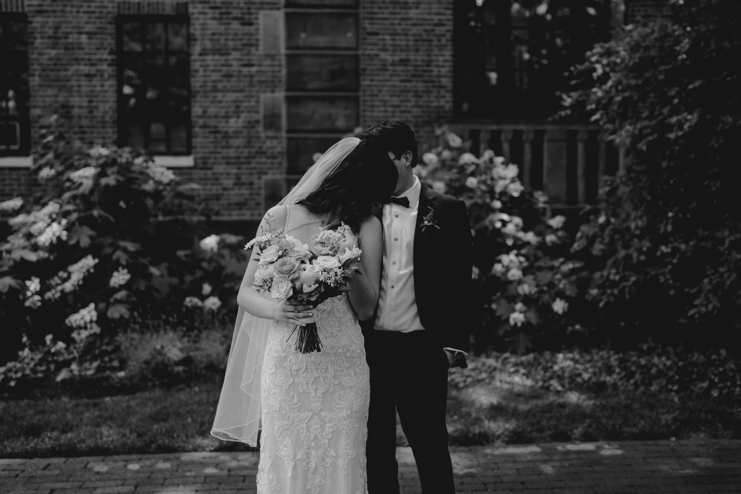 Black and white photo of bride and groom sharing intimate moment in garden setting.