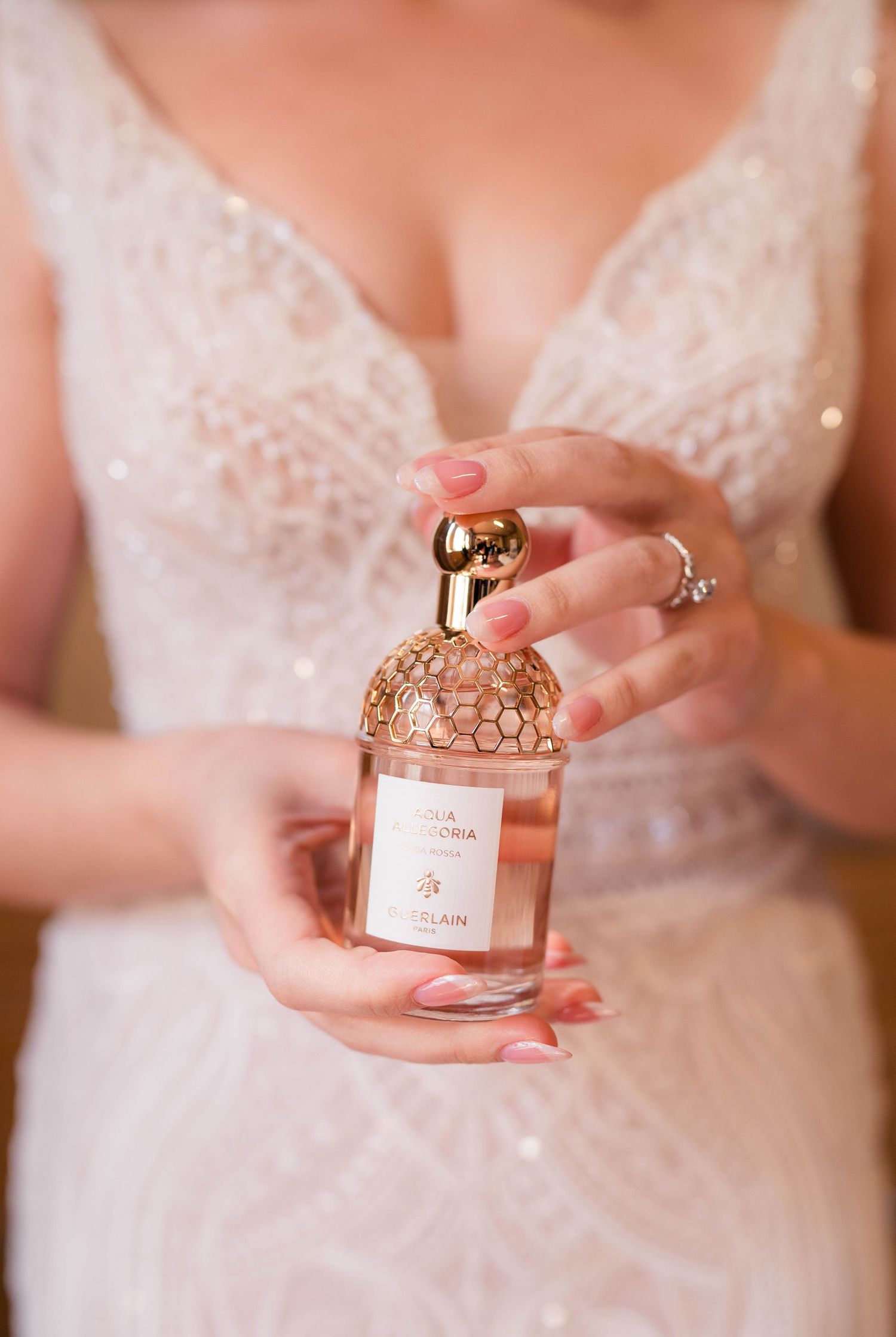 Bride holds a Guerlain Aqua Allegoria perfume bottle in her hands wearing a beaded wedding gown.