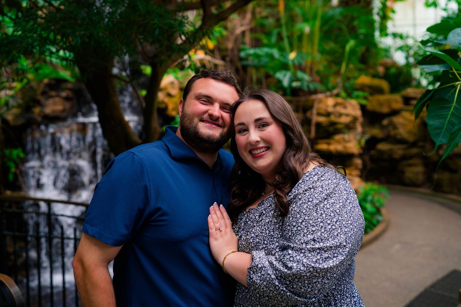 Happy newly engaged couple posing together in front of a waterfall in a tropical garden.