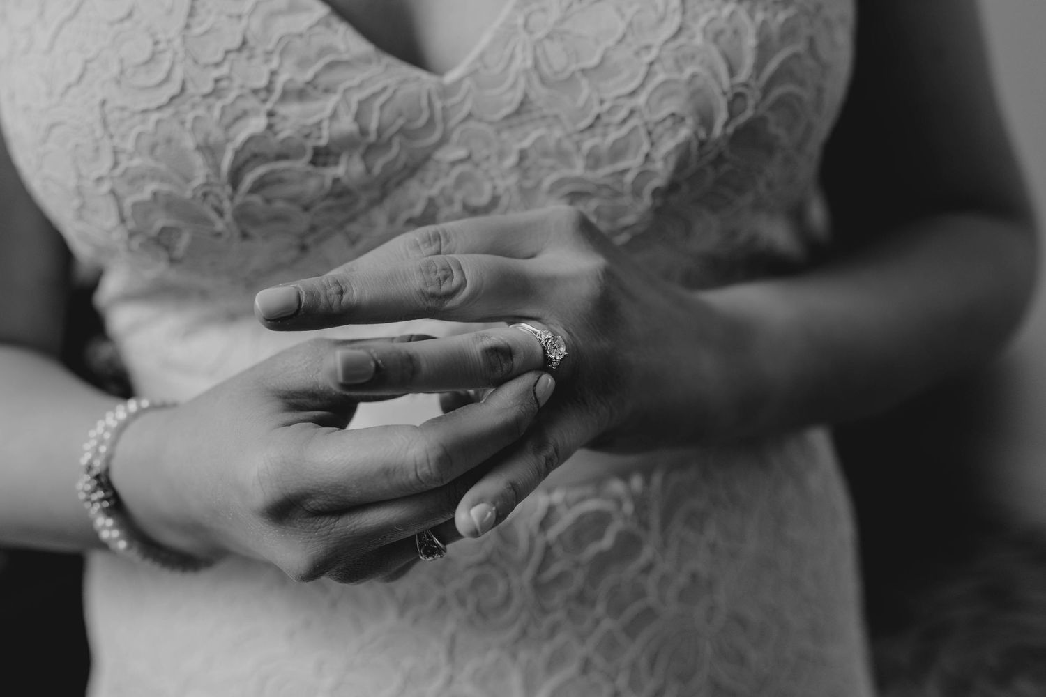 Black and white close-up of bride's hands showing pearl bracelet and diamond ring.