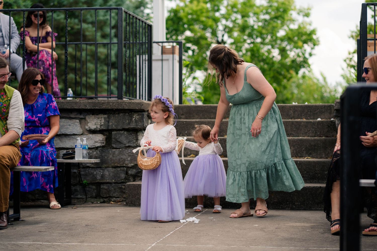 Two young flower girls in lavender tulle dresses with floral crowns walk the aisle at outdoor wedding ceremony.