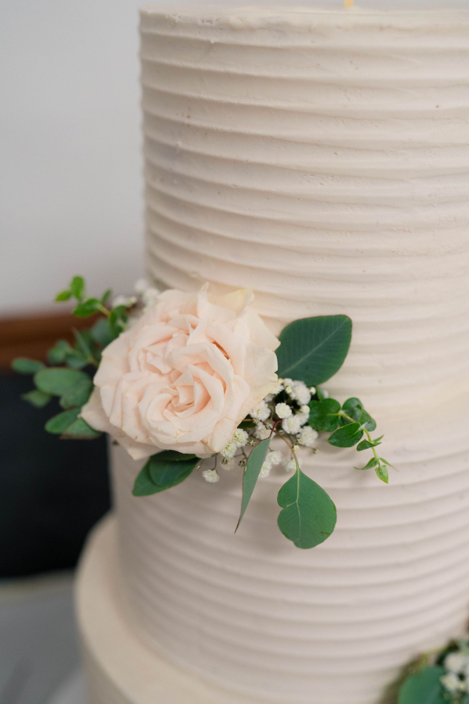 Elegant three-tier white ribbed wedding cake decorated with blush pink roses and green eucalyptus leaves.