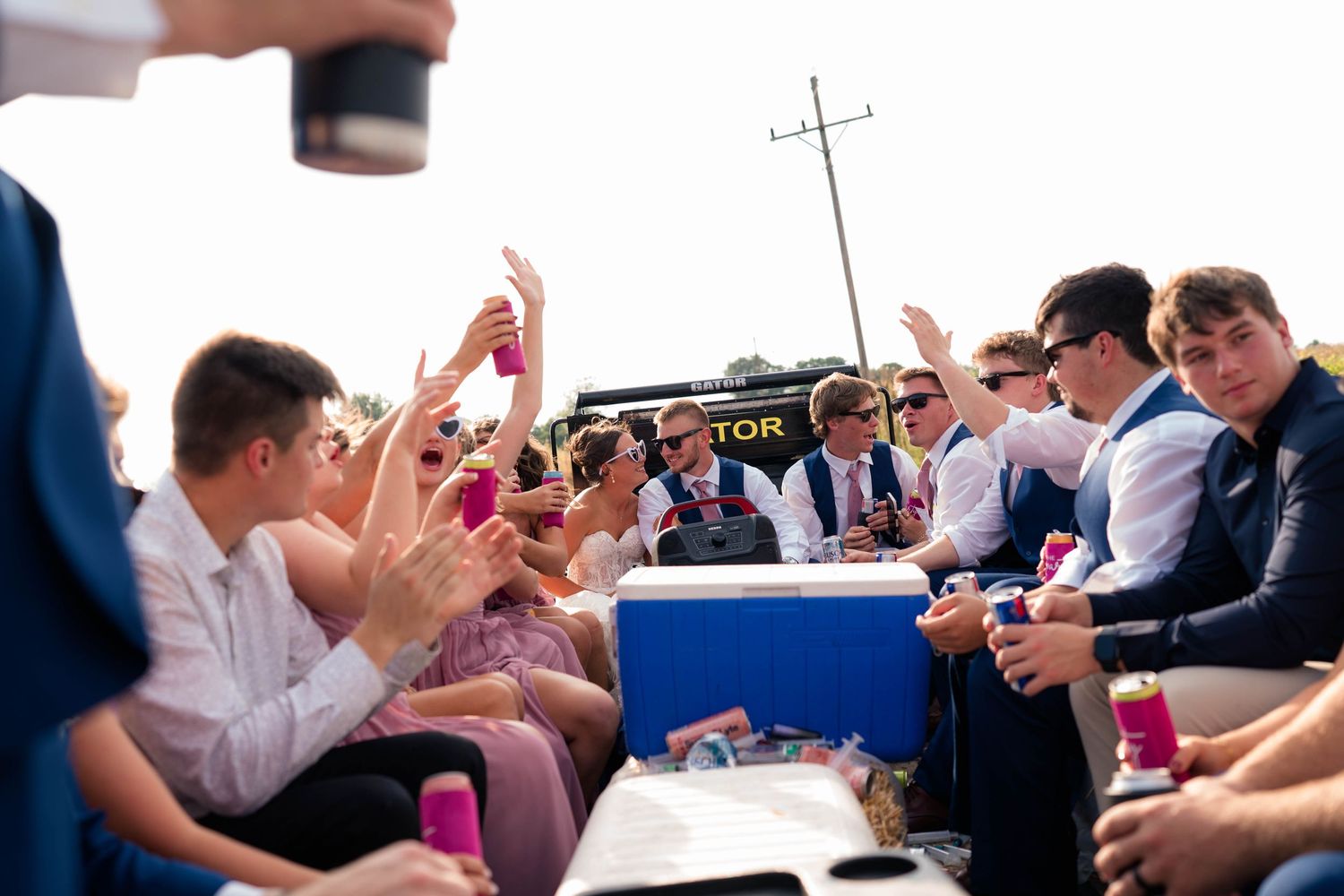 Wedding guests raise hands and celebrate on truck bed with blue cooler at outdoor wedding reception.