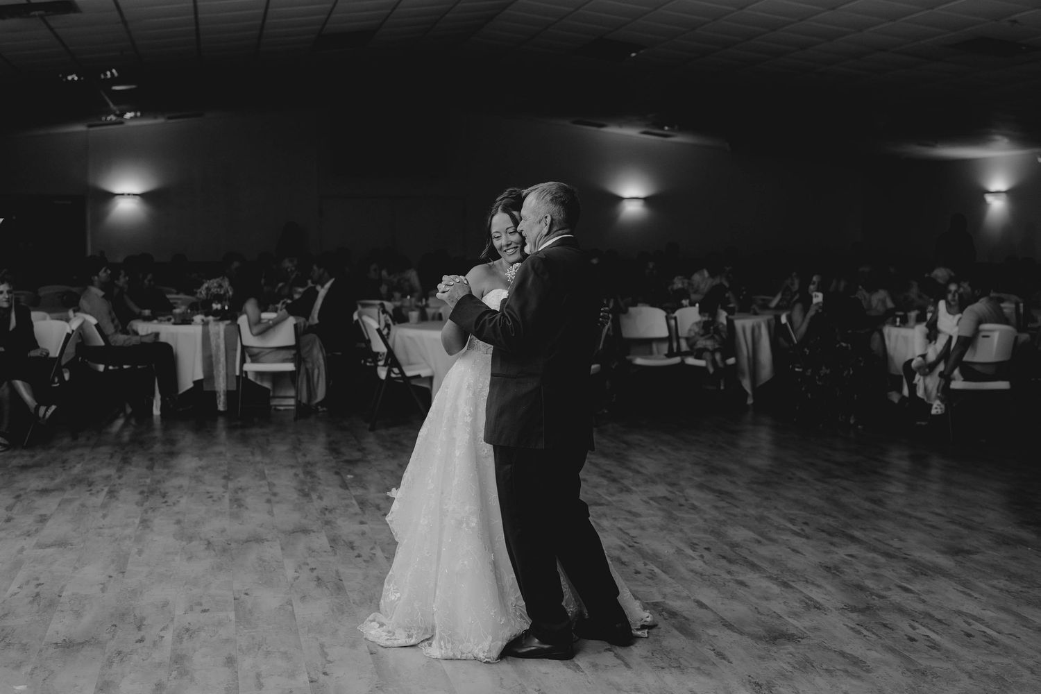 Bride and groom share first dance in black and white photo at elegant wedding reception venue.
