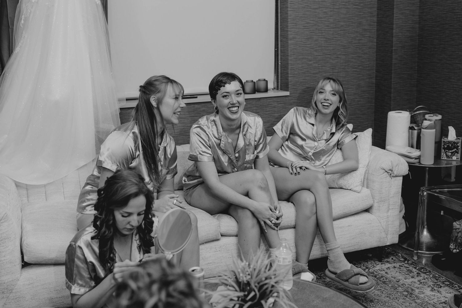 Black and white photo of bridesmaids laughing together in satin robes before a wedding.