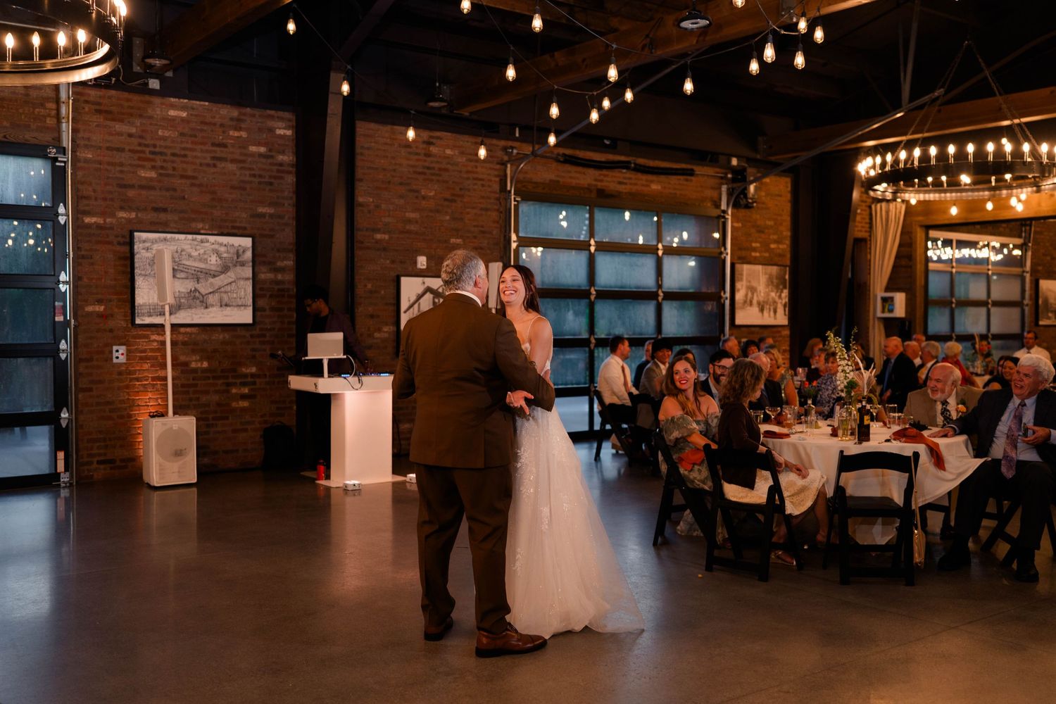 Bride and groom share intimate first dance in warmly lit rustic industrial wedding reception venue.