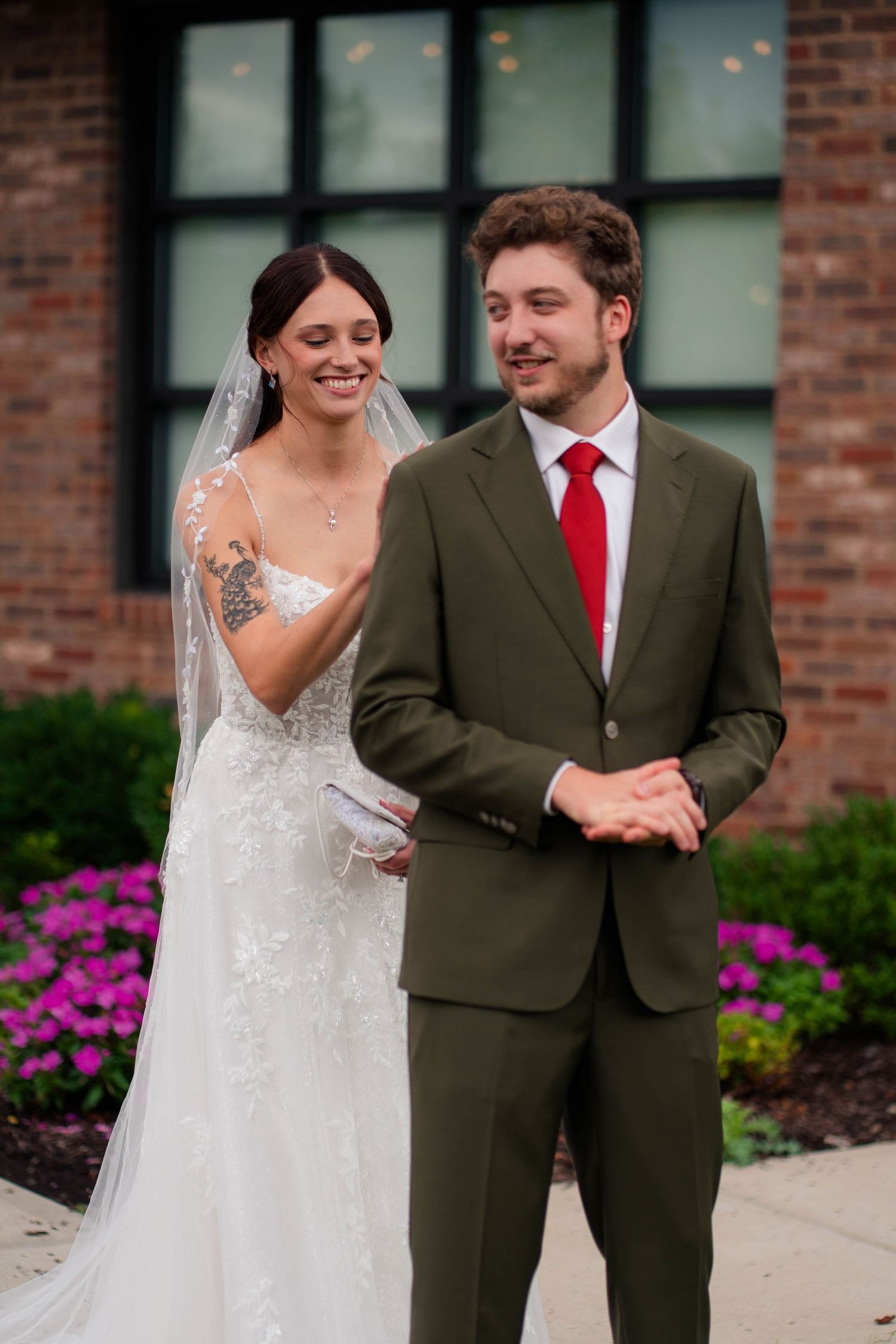 Bride in lace gown with veil and groom in olive suit sharing first look moment.