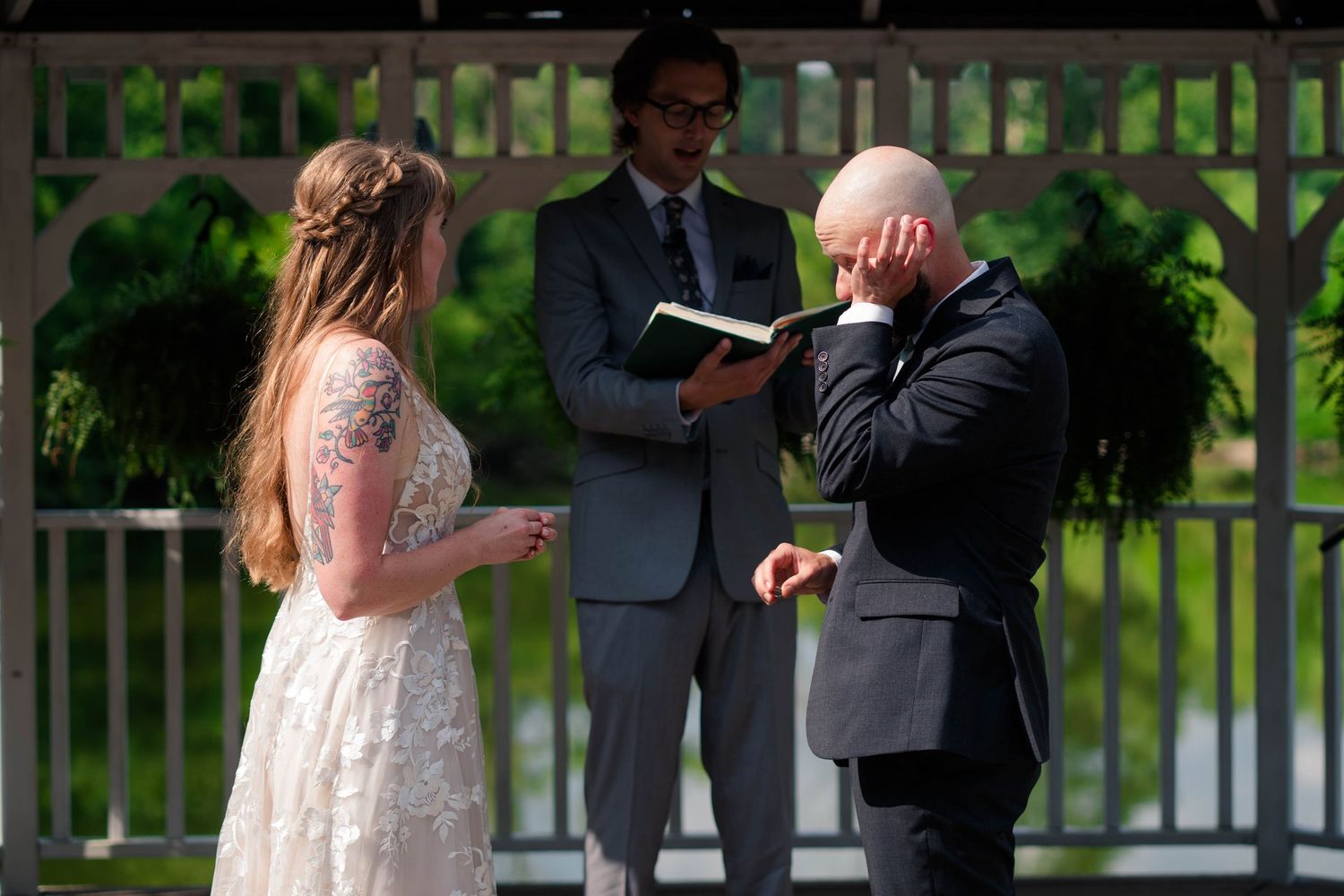 Emotional groom covers his face during outdoor gazebo wedding ceremony while bride and officiant stand beside him.